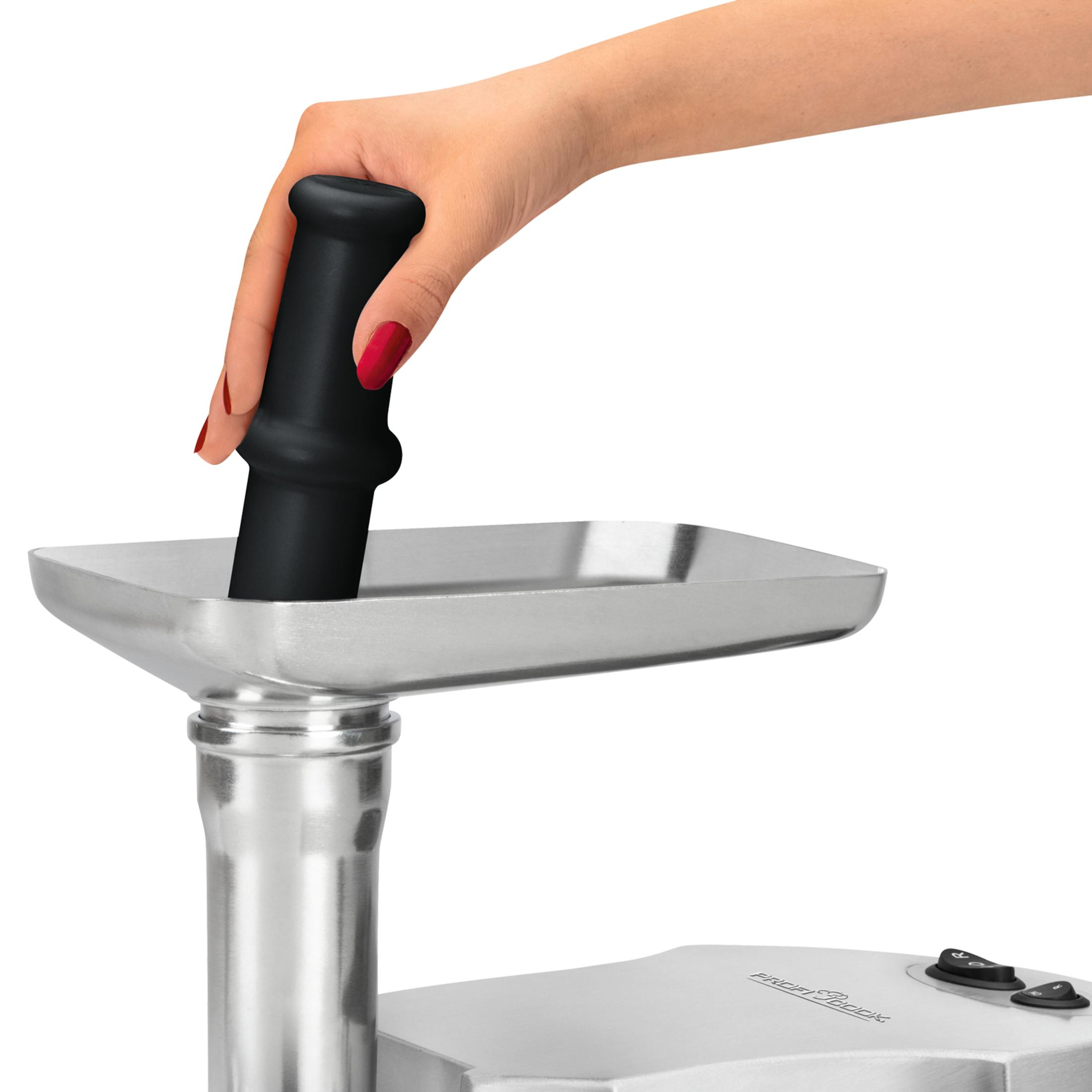 Una mano con esmalte de uñas rojo empuja un émbolo negro en una picadora de carne.