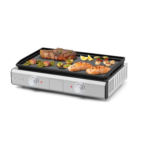 Ein silberner Tischgrill mit Steaks, Lachs, Spargel und Zitronenspalten.