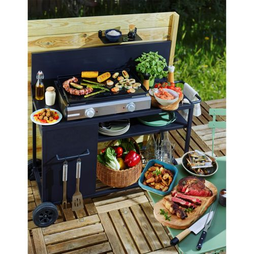Grill mit gegrillten Speisen, Fleisch, Gemüse und Beilagen auf einer Holzterrasse.