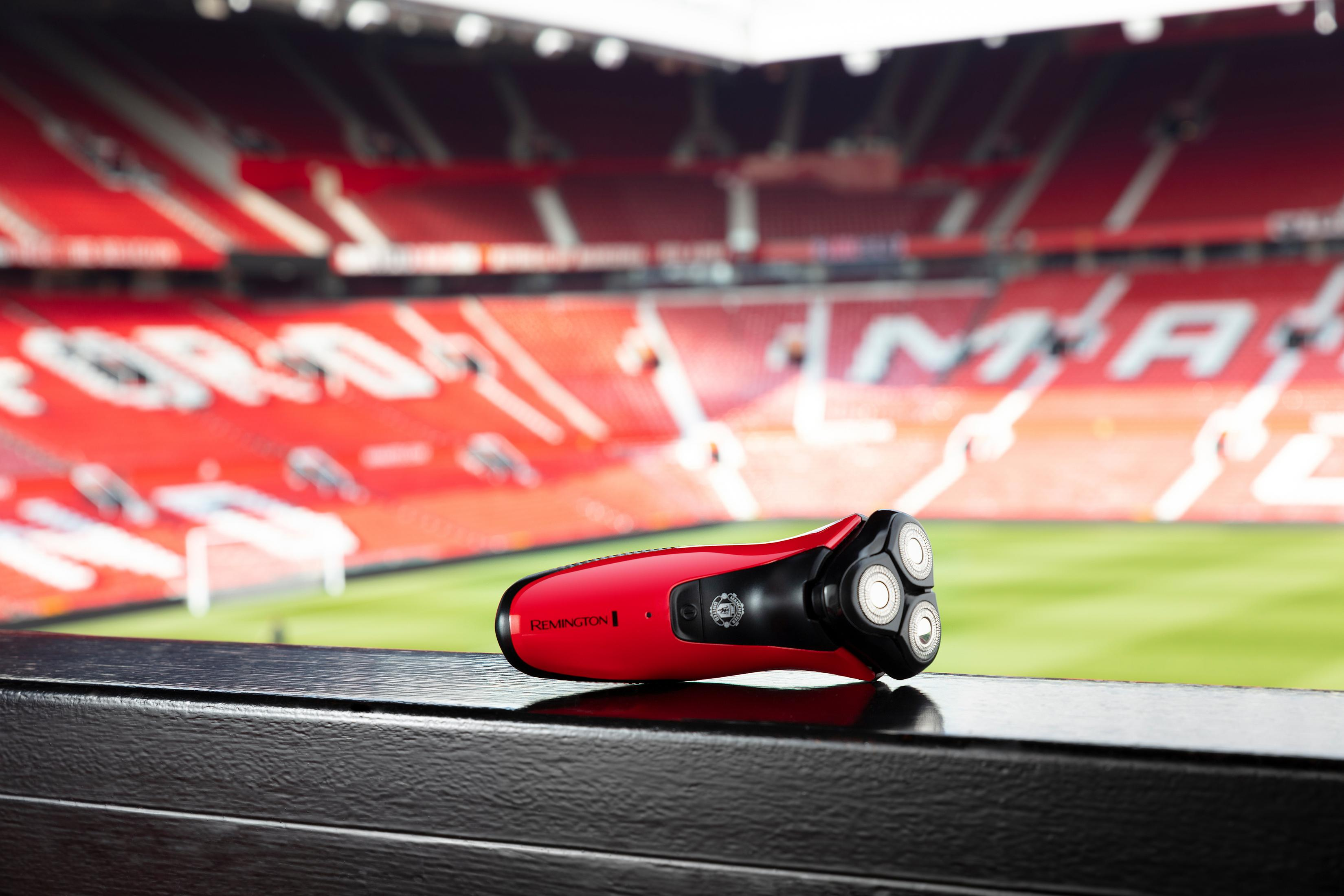 Una afeitadora Remington roja descansa sobre una superficie oscura frente a un estadio de fútbol.
