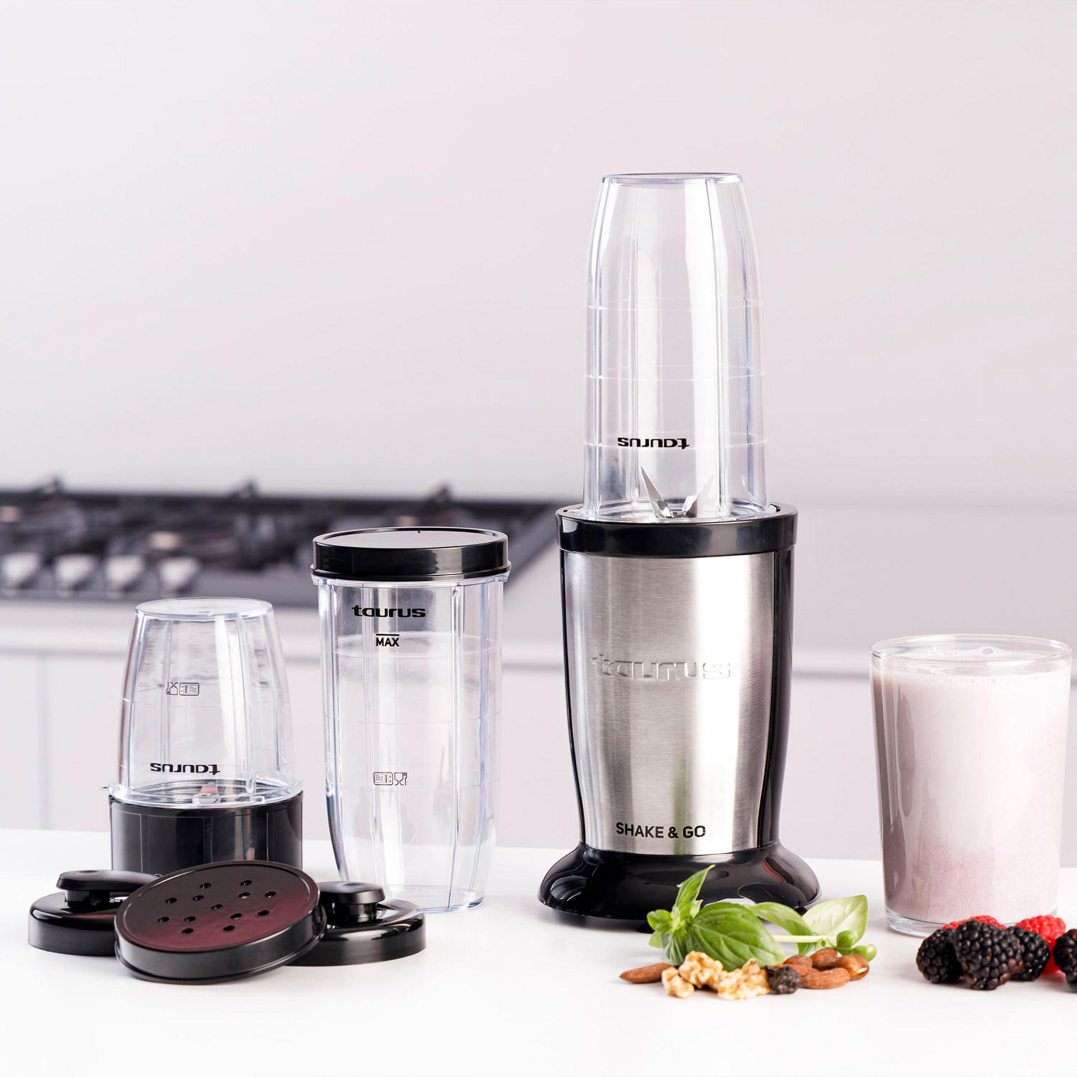 Ein Standmixer mit Zubehör, Beeren und Nüssen auf einem weißen Tisch.
