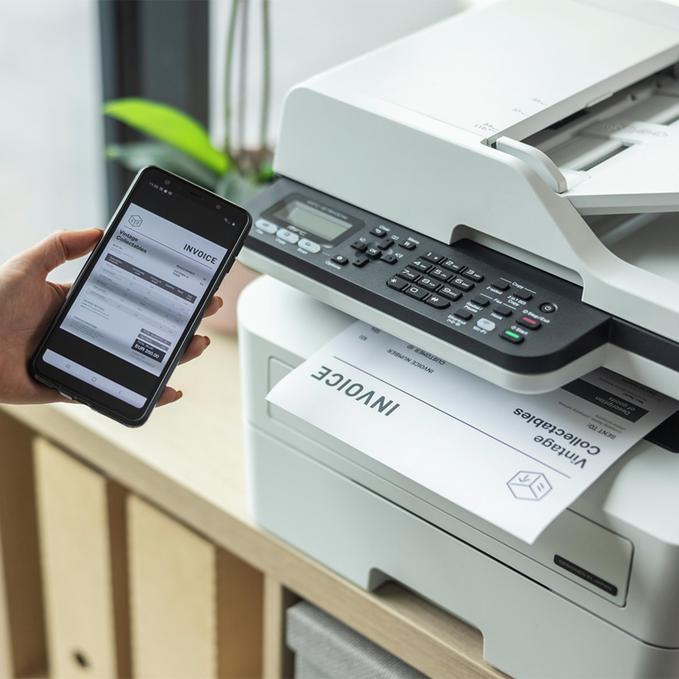 Una mano tiene uno smartphone con una fattura, accanto a una stampante che stampa una fattura.