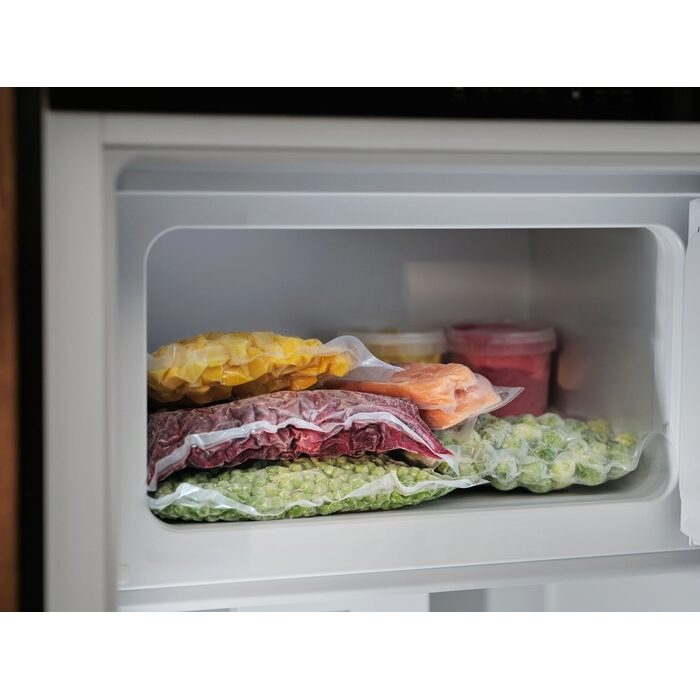 Cajón del congelador lleno de bolsas de verduras y carne congeladas.