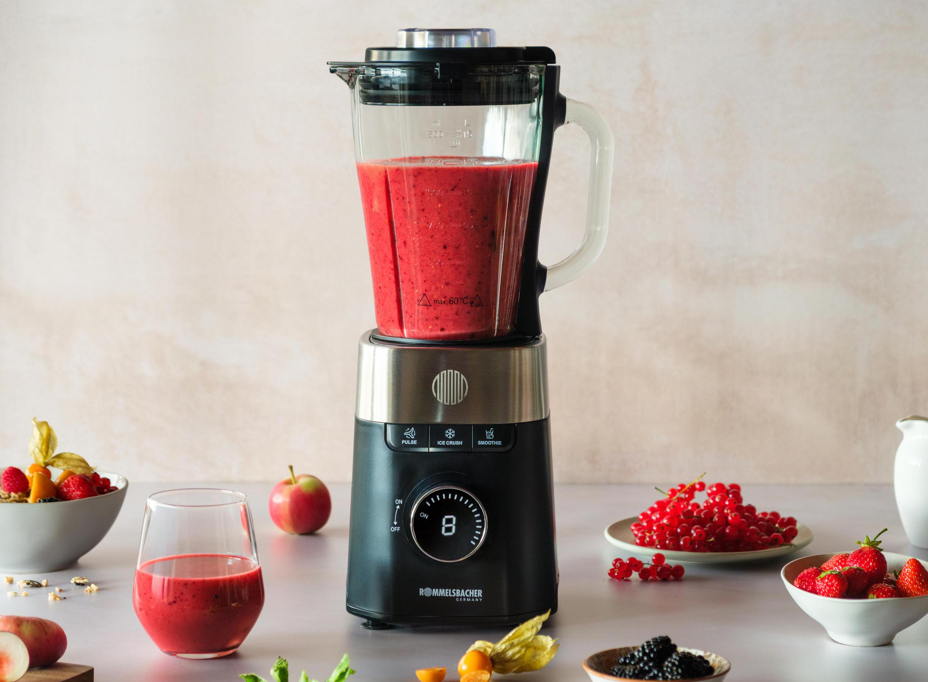 Un frullatore nero con frullato rosso, circondato da frutta e un bicchiere di frullato.