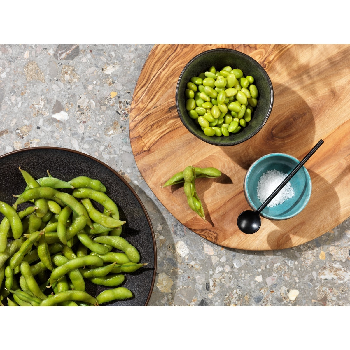 Fagioli edamame in baccelli e sgusciati, vicino a sale e cucchiaio.