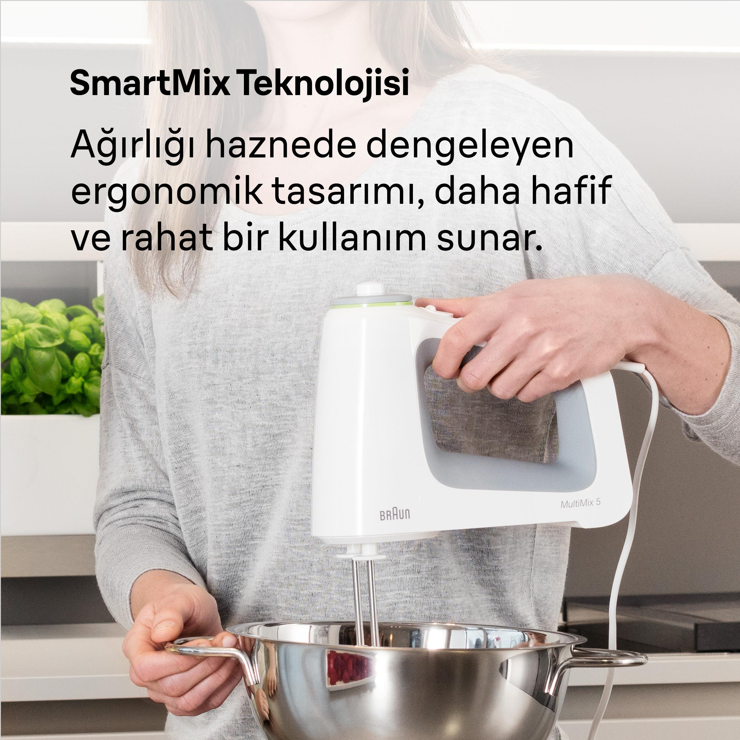 Kadın, paslanmaz çelik kase üzerinde beyaz el mikseri tutuyor. Arkada yeşil bitkiler var.