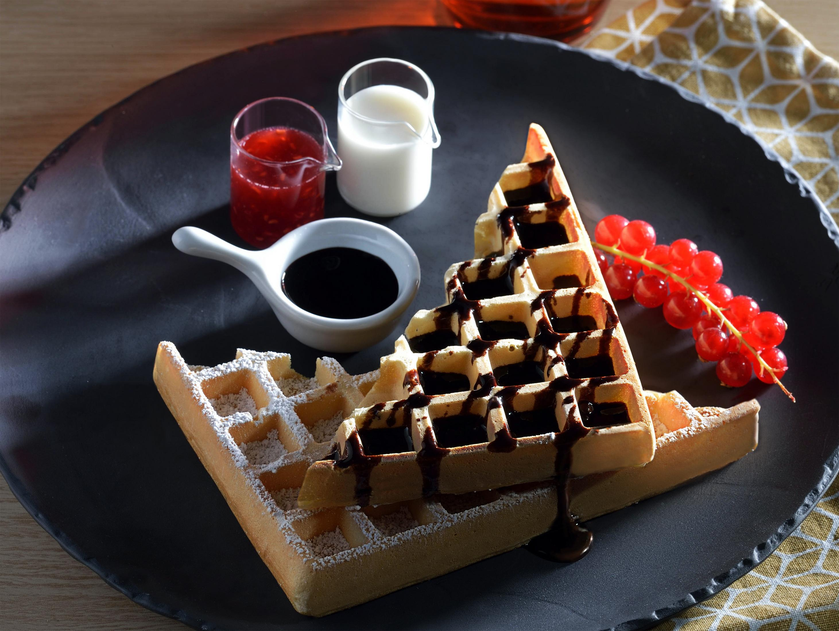 Waffeln mit Schokoladensauce, Beeren und Milch auf einem schwarzen Teller.
