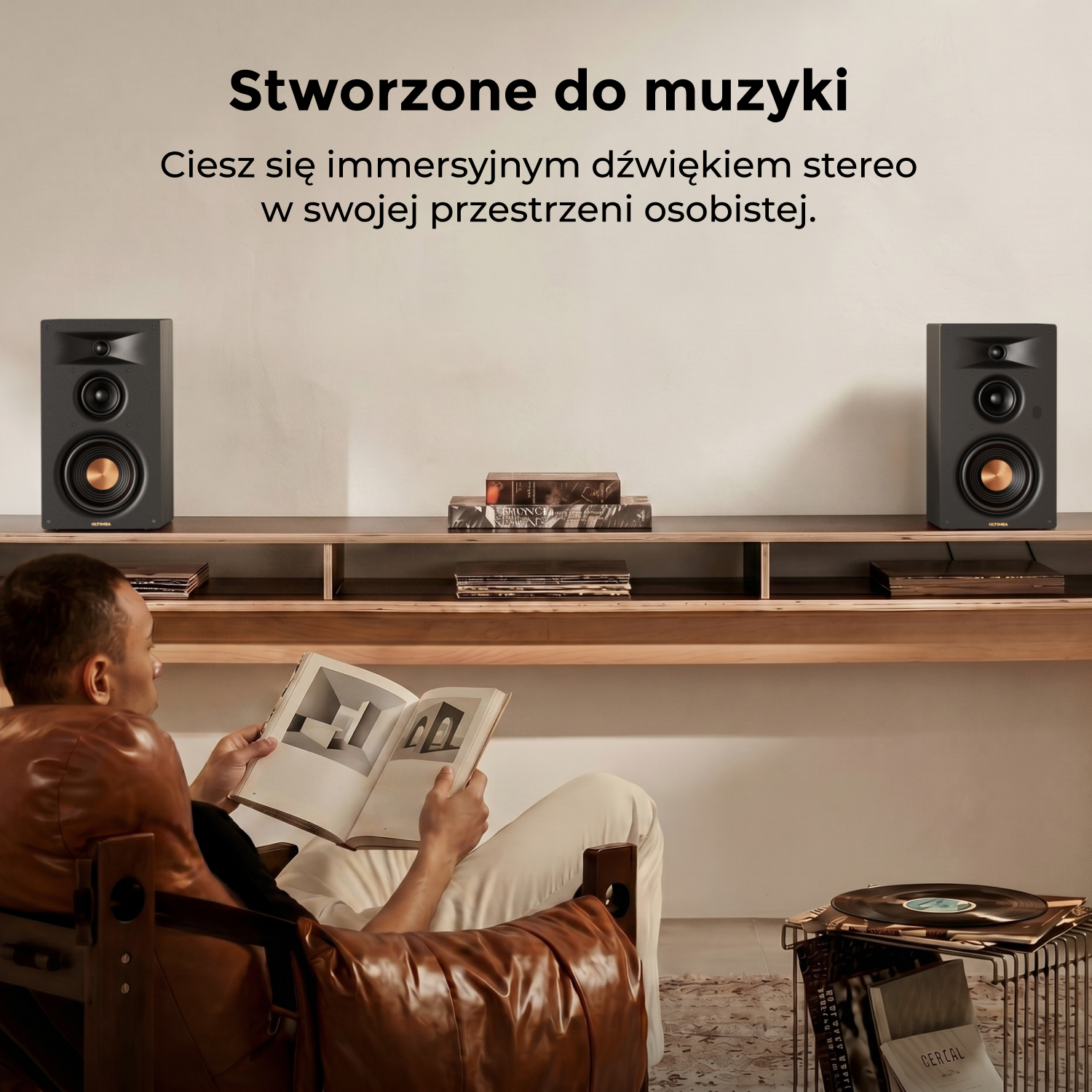 Mężczyzna czyta książkę w fotelu, dwa czarne głośniki na półce.