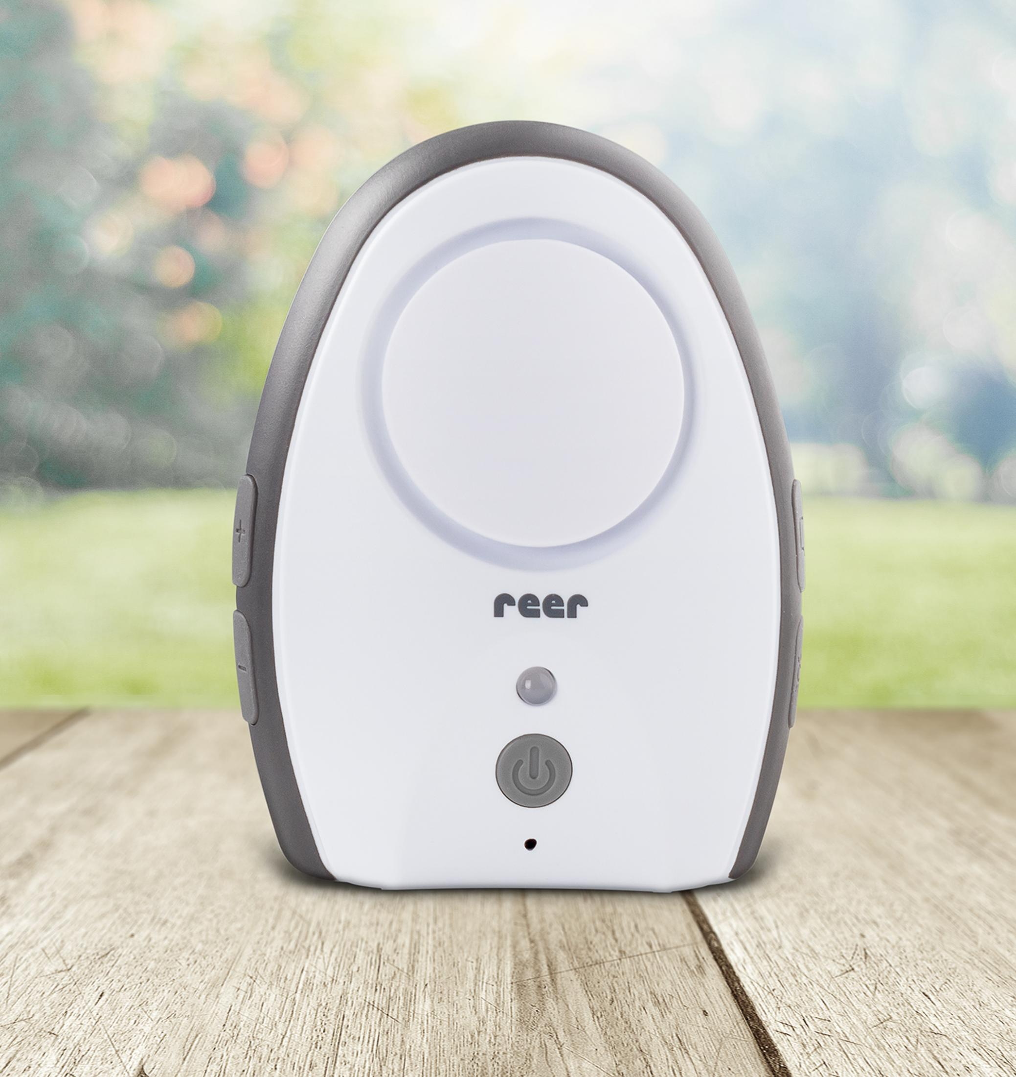 Un baby monitor bianco con bordo grigio su tavolo di legno, sfondo sfocato.