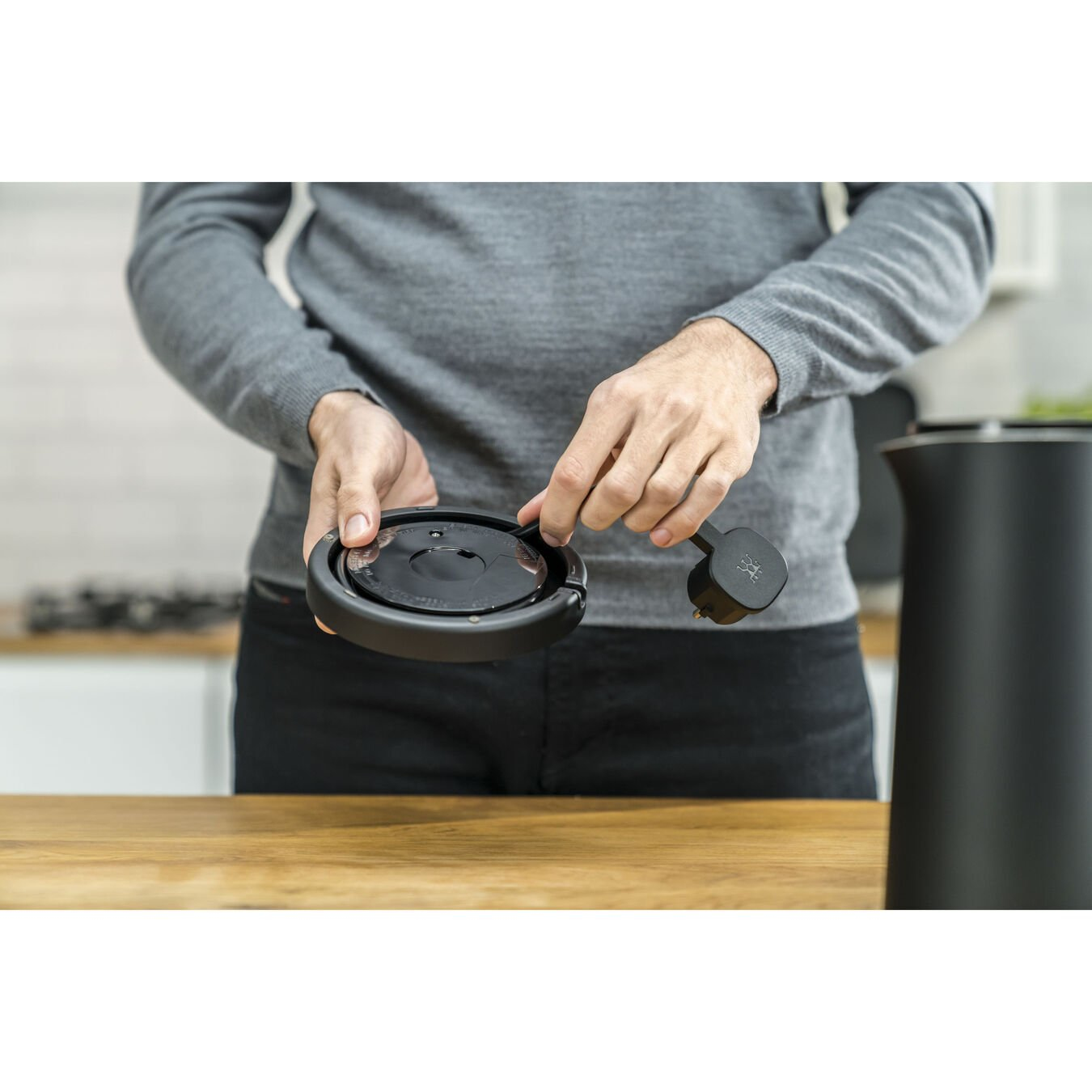 Mann hält schwarzen Wasserkocherdeckel mit Stecker in der Hand.