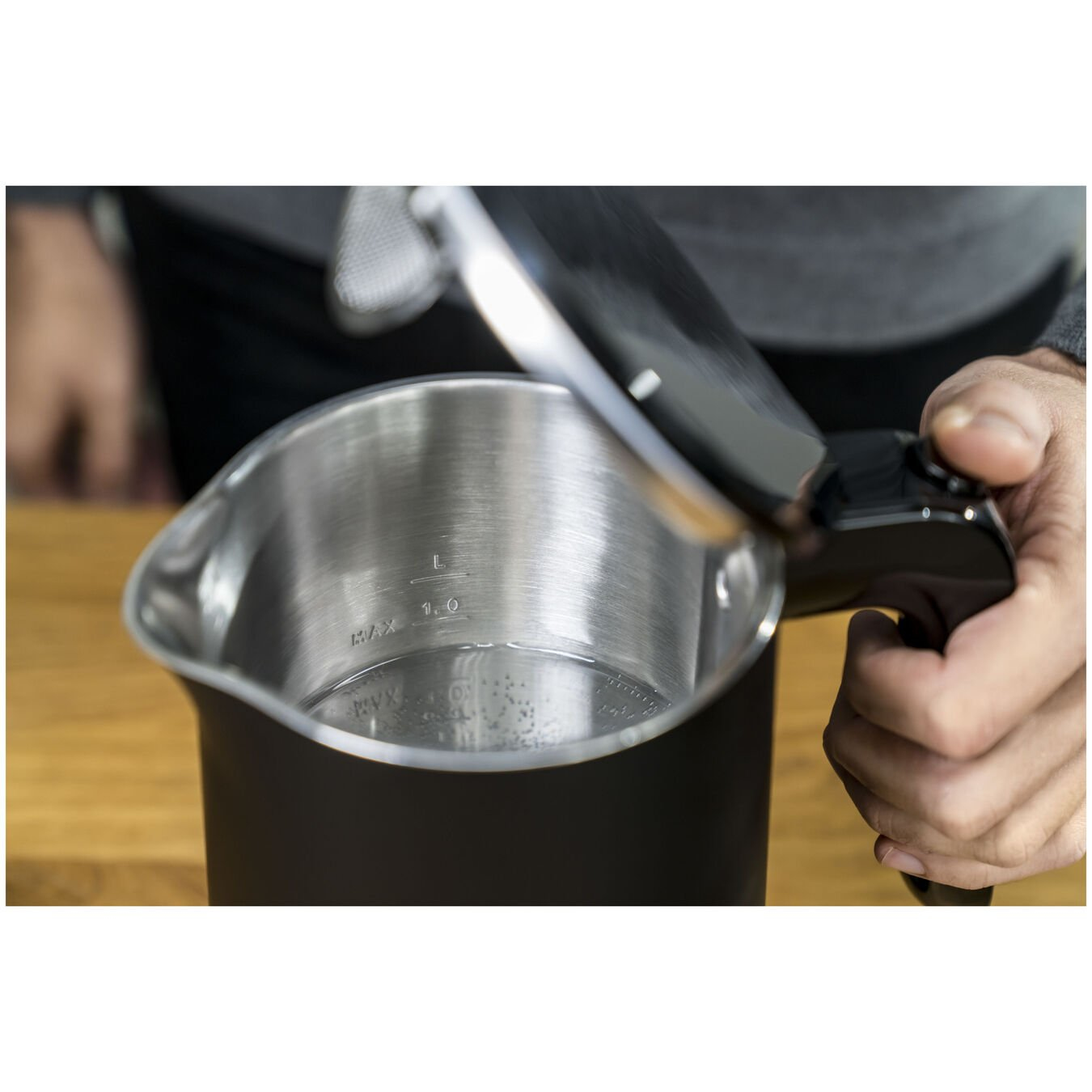 Eine Hand öffnet den Deckel eines Wasserkochers mit sichtbarem Wasserstand.