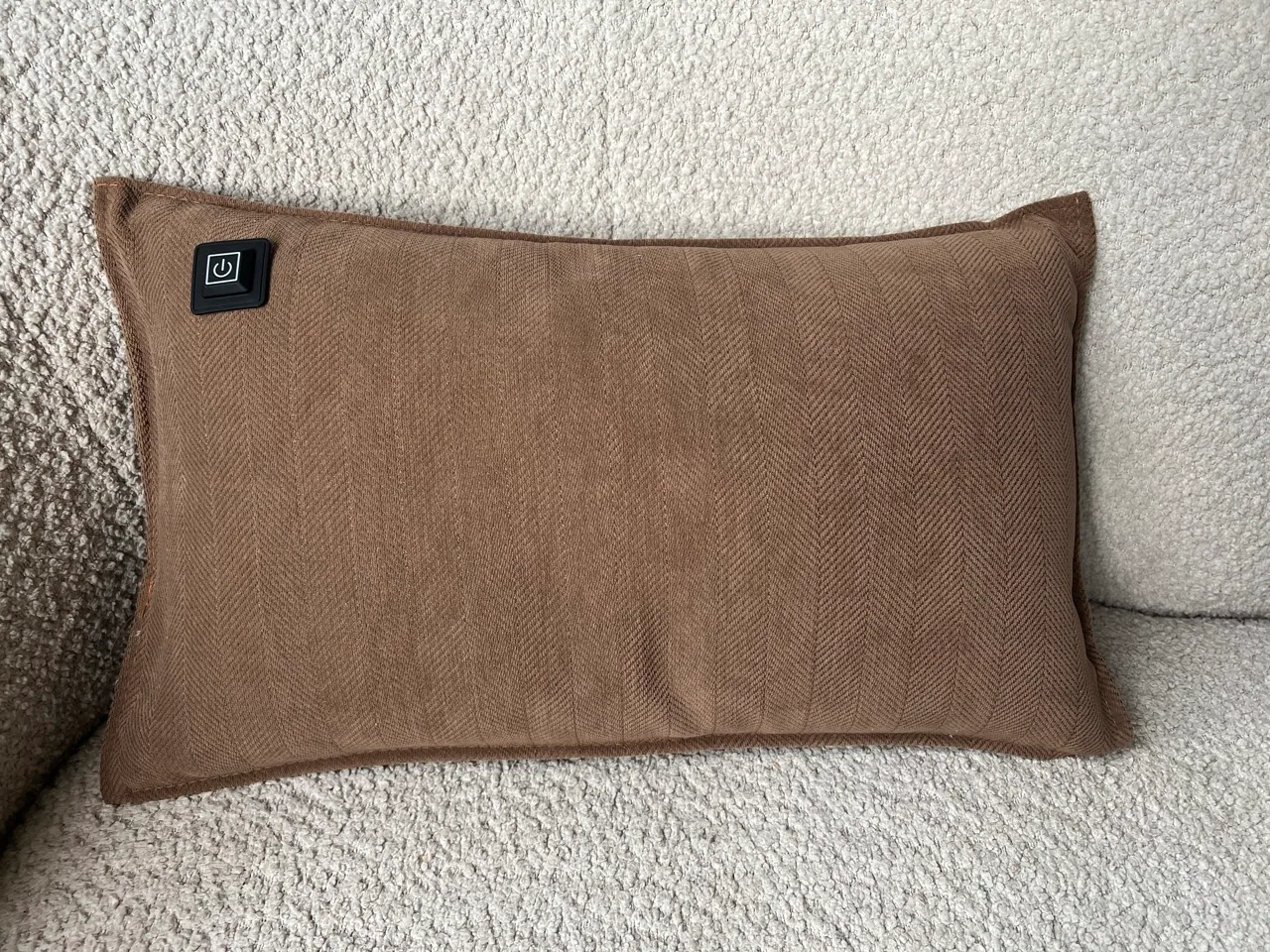 Ein braunes Kissen mit Fischgrätenmuster und einem schwarzen Ein-/Ausschaltknopf.