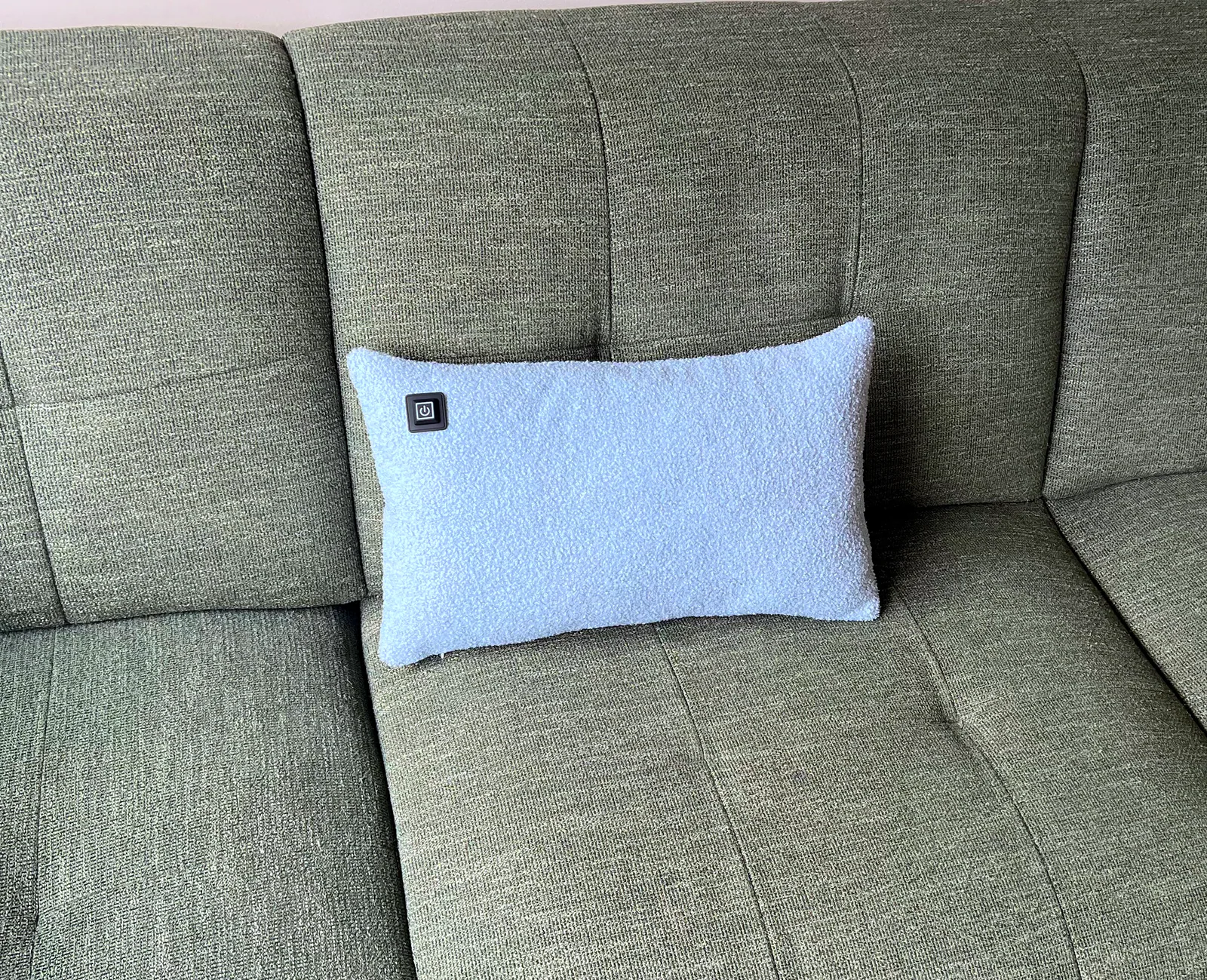 Ein hellblaues Kissen mit einem schwarzen Stromsymbol liegt auf einer grünen Couch.