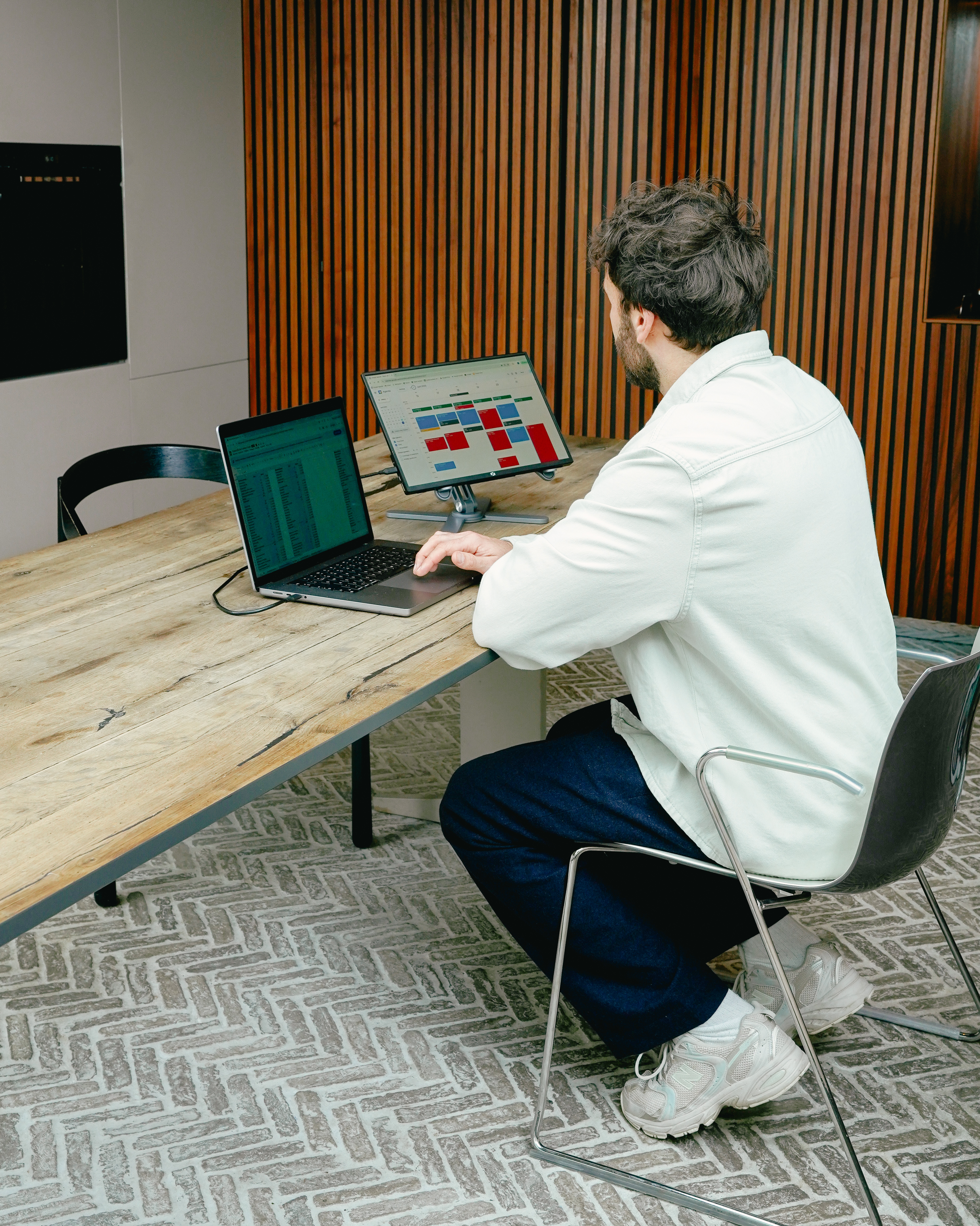 Homme en veste claire travaille sur ordinateur portable et tablette dans bureau moderne boisé.