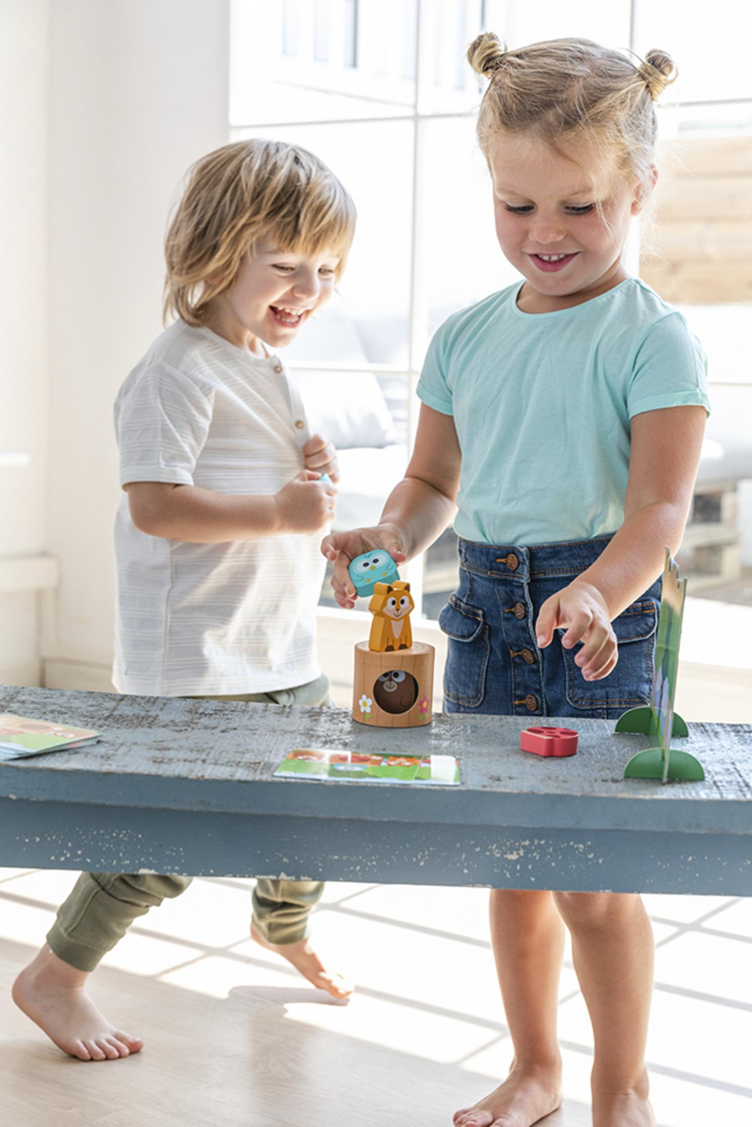 Dos niños juegan con juguetes de madera sobre una mesa.