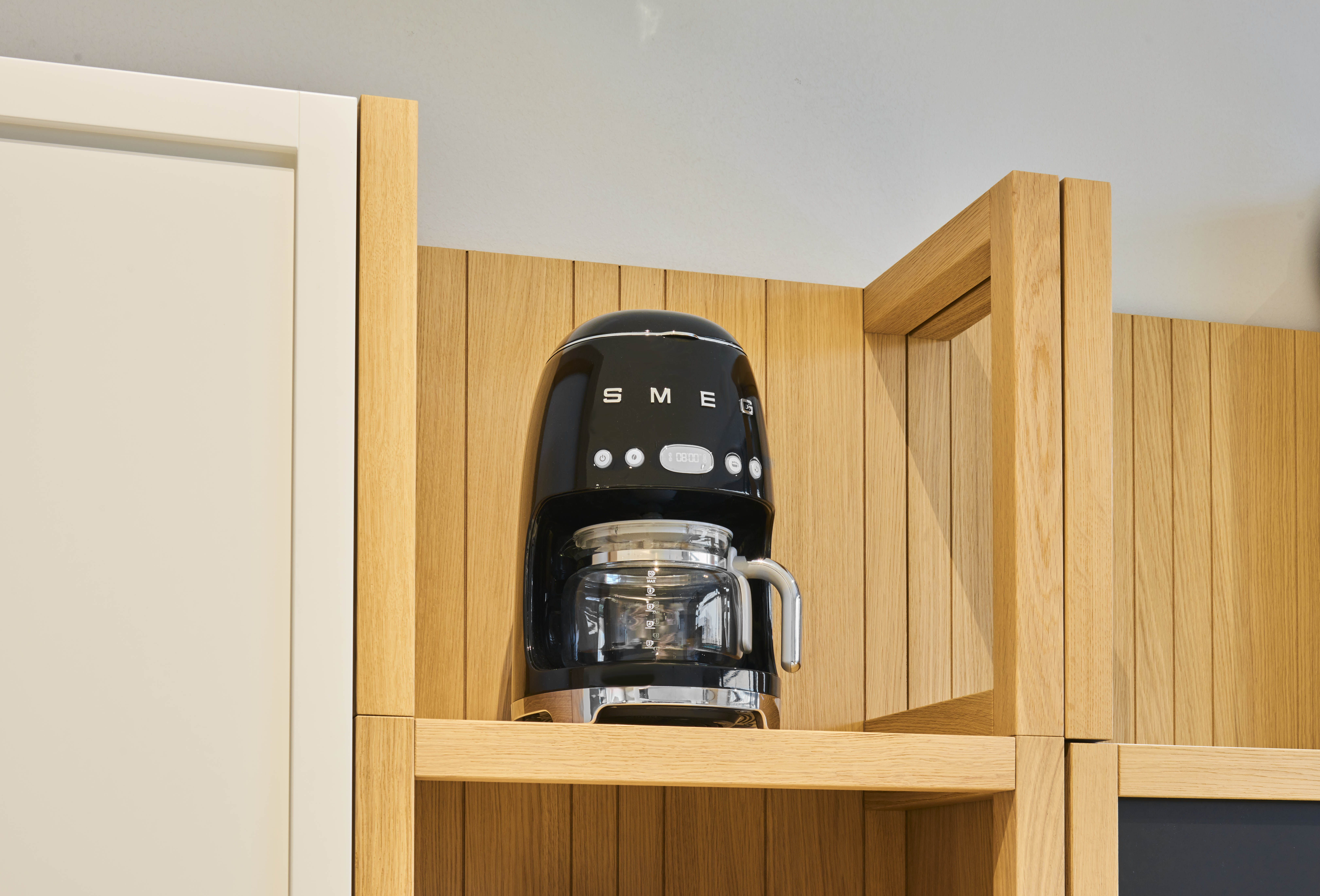 Schwarzer SMEG-Kaffeemaschine mit Glaskanne auf einem Holzregal.