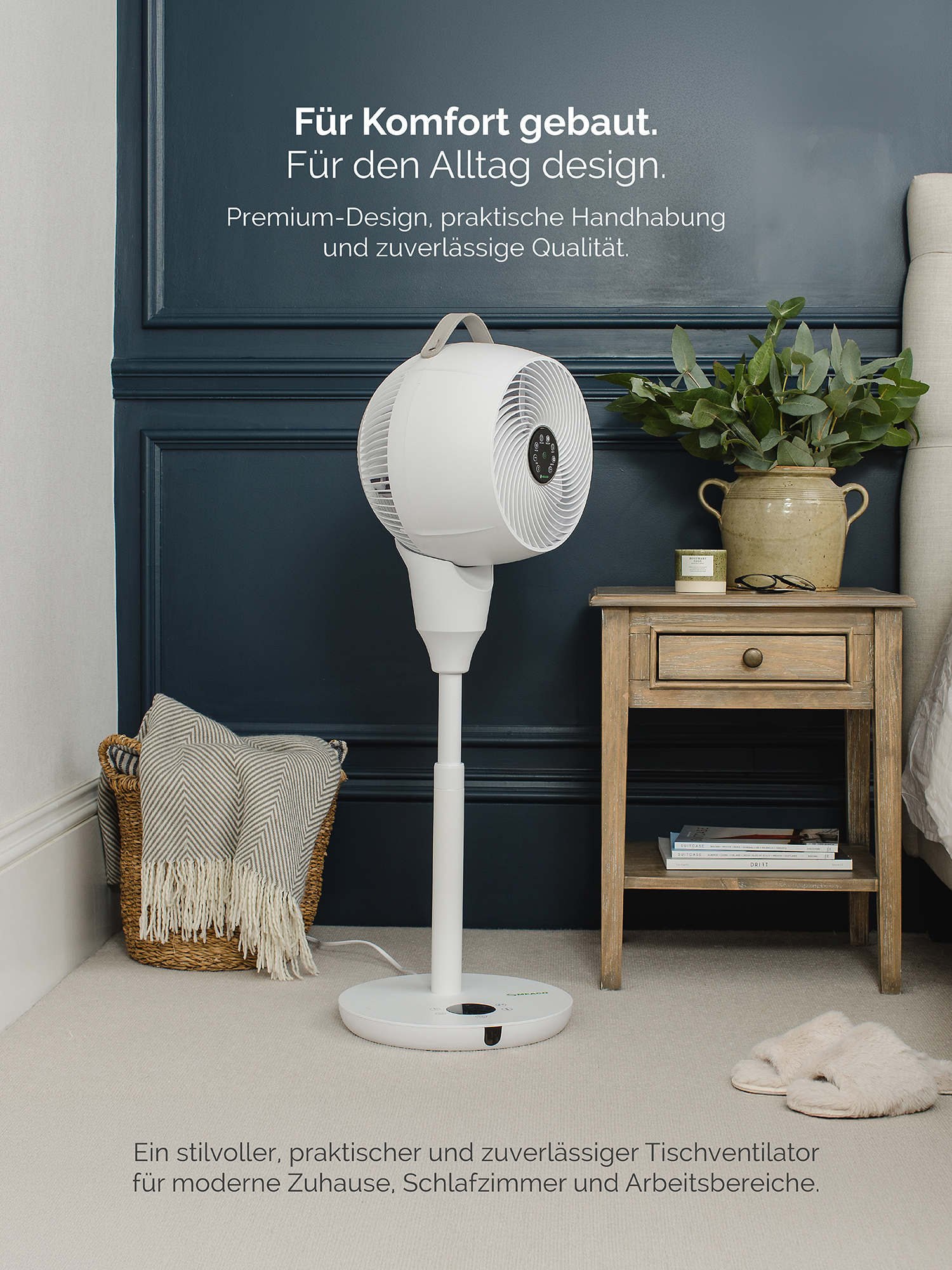 Un ventilatore da terra bianco accanto a un comodino con piante e libri.