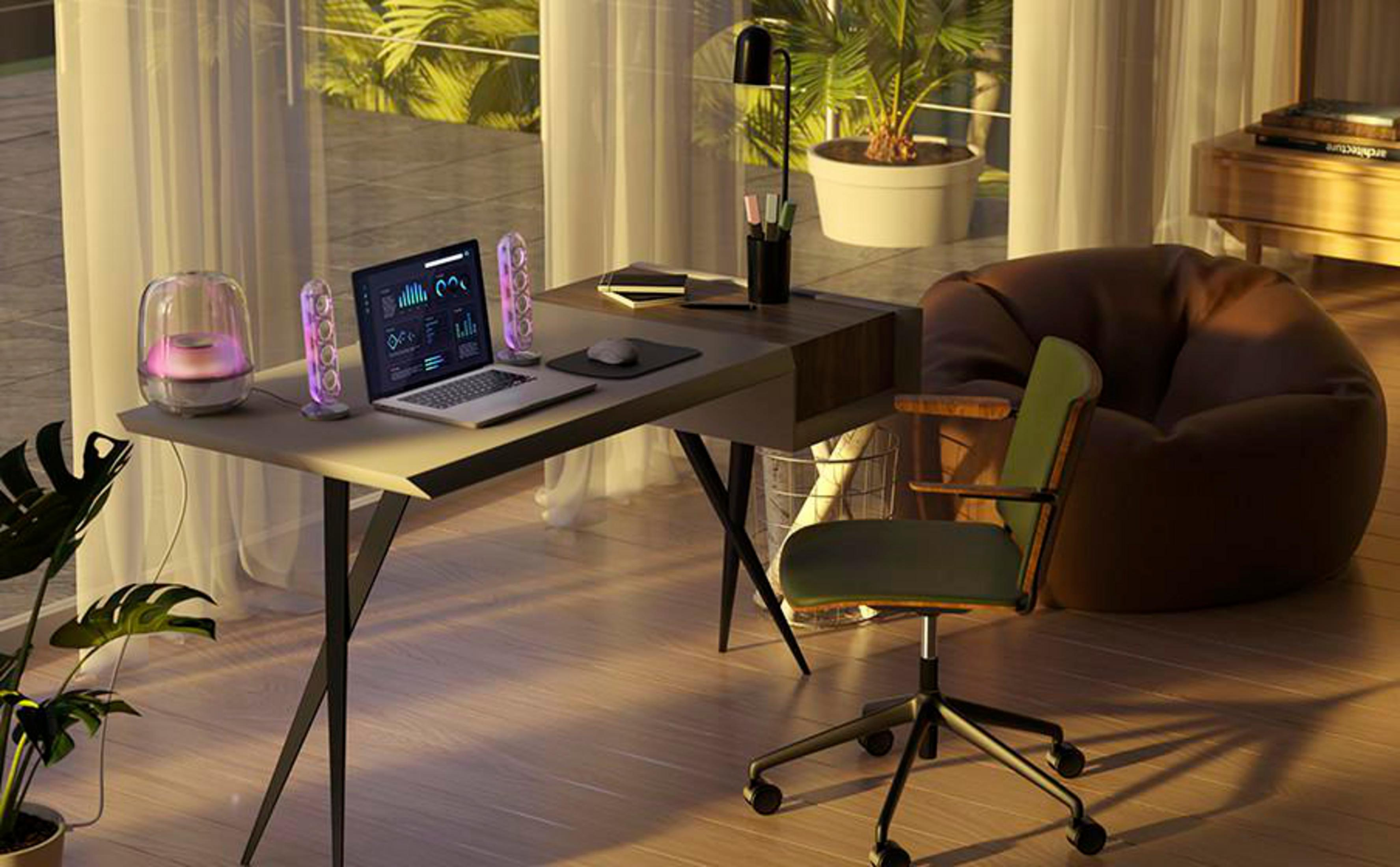 Ein Schreibtisch mit Laptop, Lautsprechern und Lampe neben einem Fenster.
