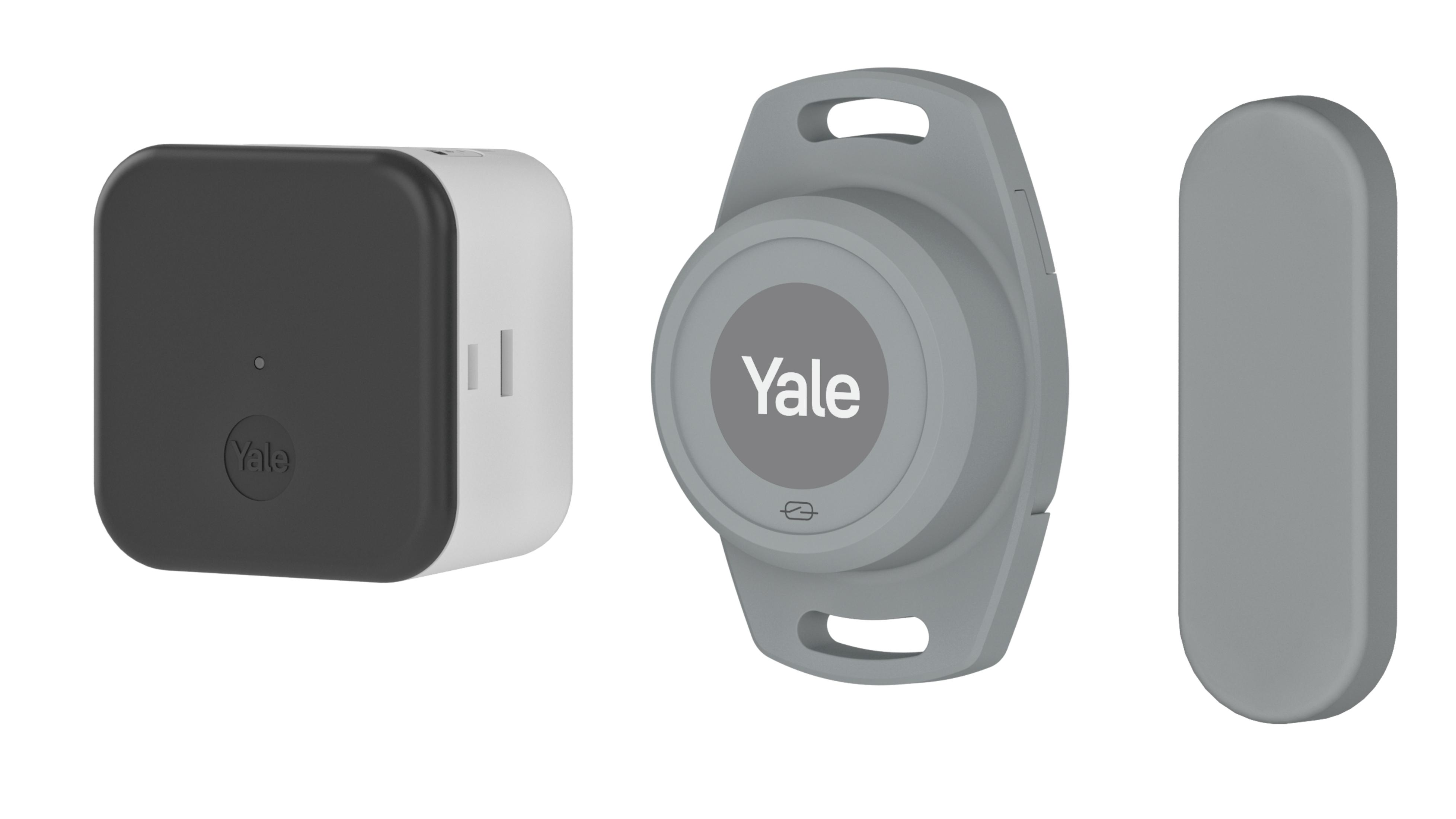 Tres dispositivos Yale en blanco: una caja negra, un llavero gris y un objeto gris alargado.