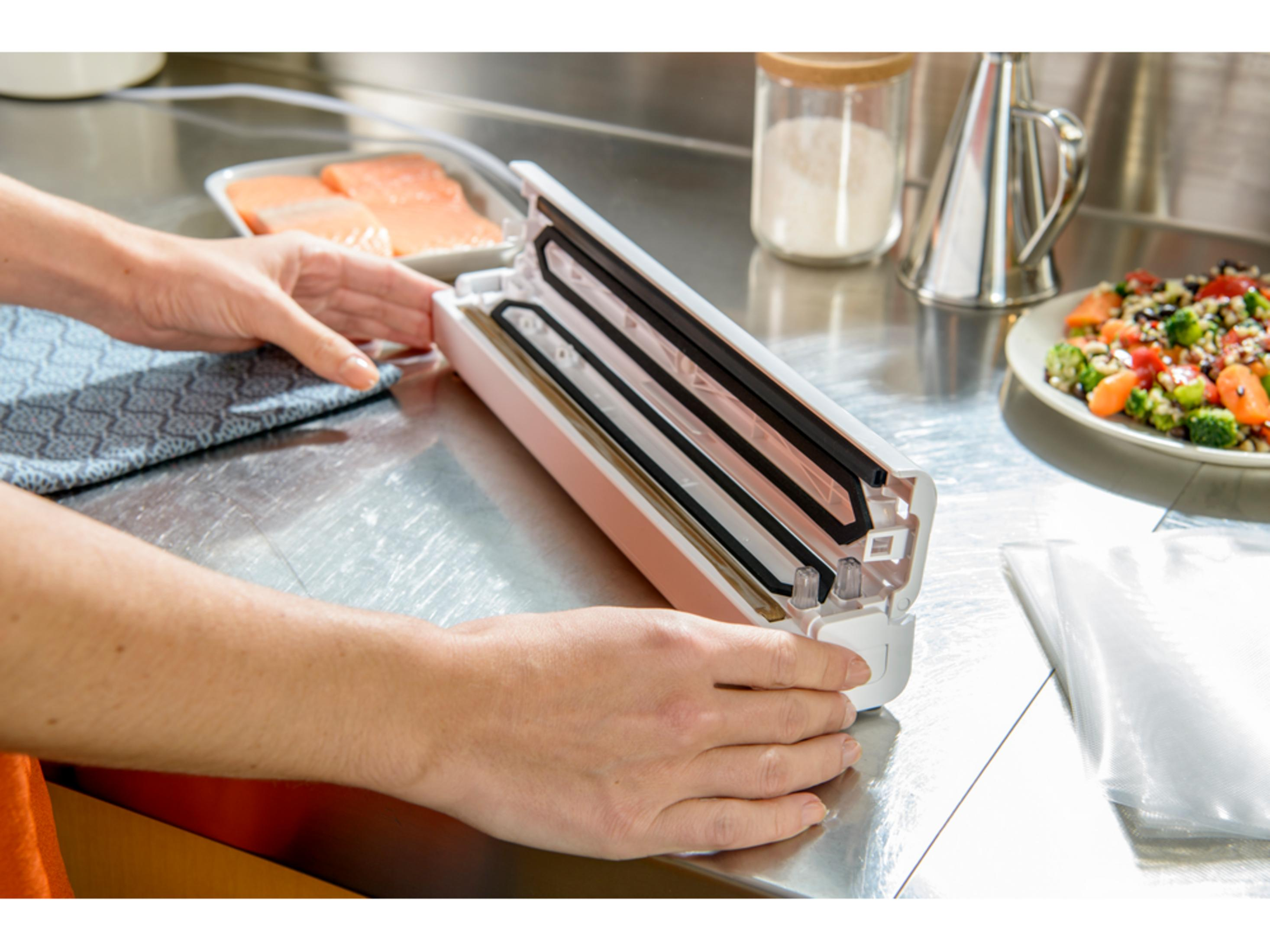Manos operando una envasadora al vacío junto a salmón y ensalada.