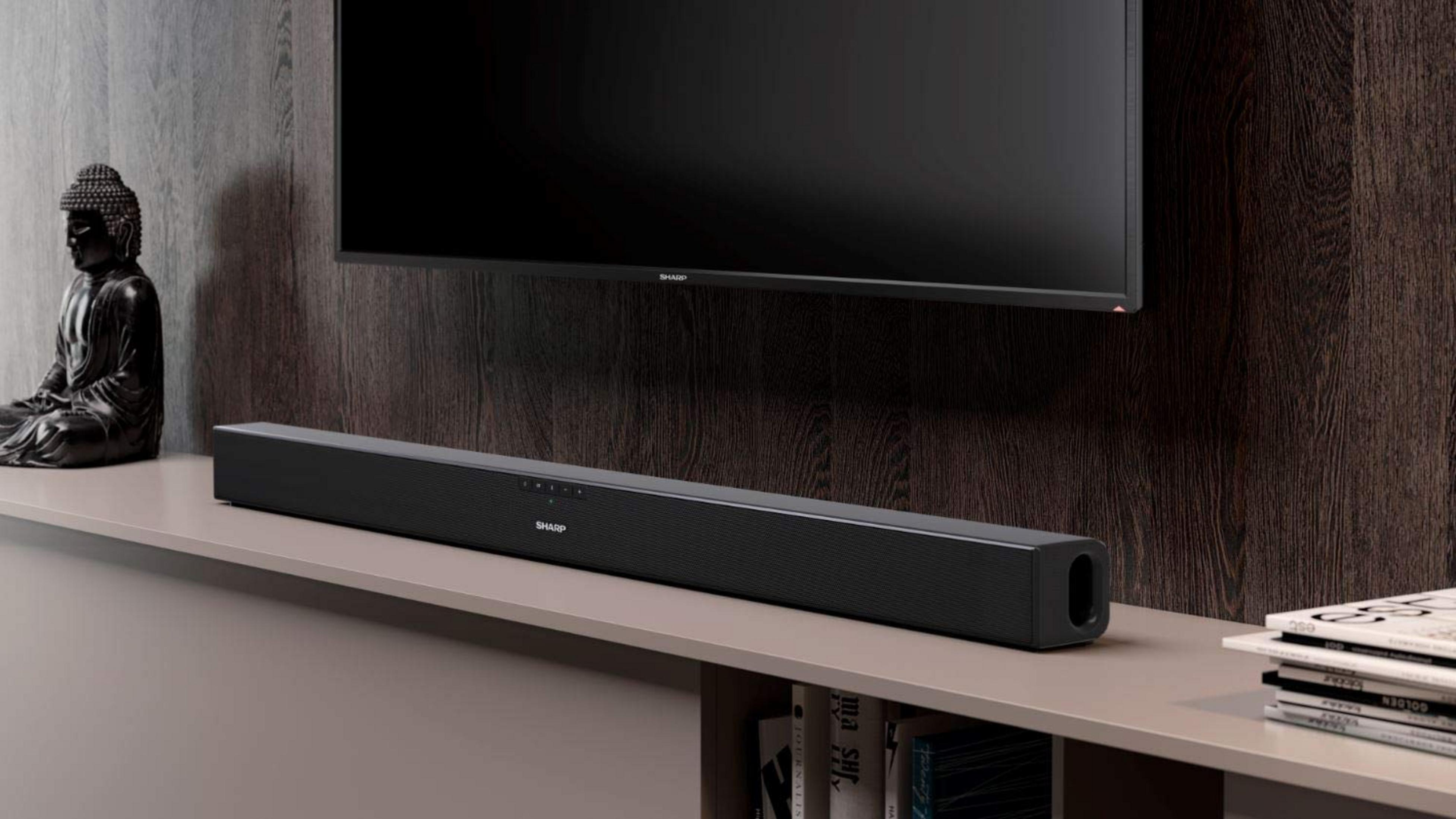 Una barra de sonido negra está sobre un estante debajo de un televisor, con una estatua de Buda cerca.