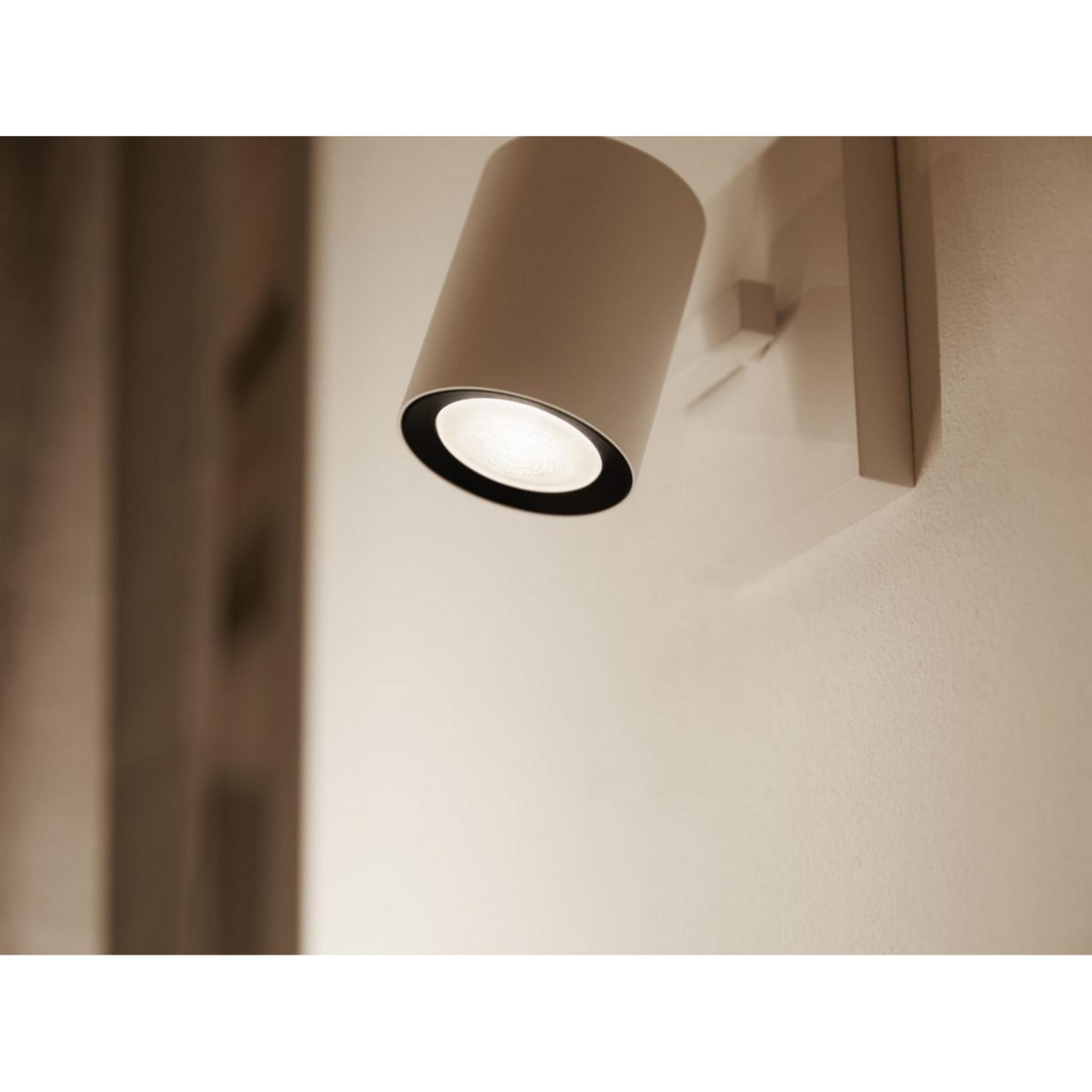 Eine weiße zylindrische Wandleuchte mit schwarzem Ring leuchtet.