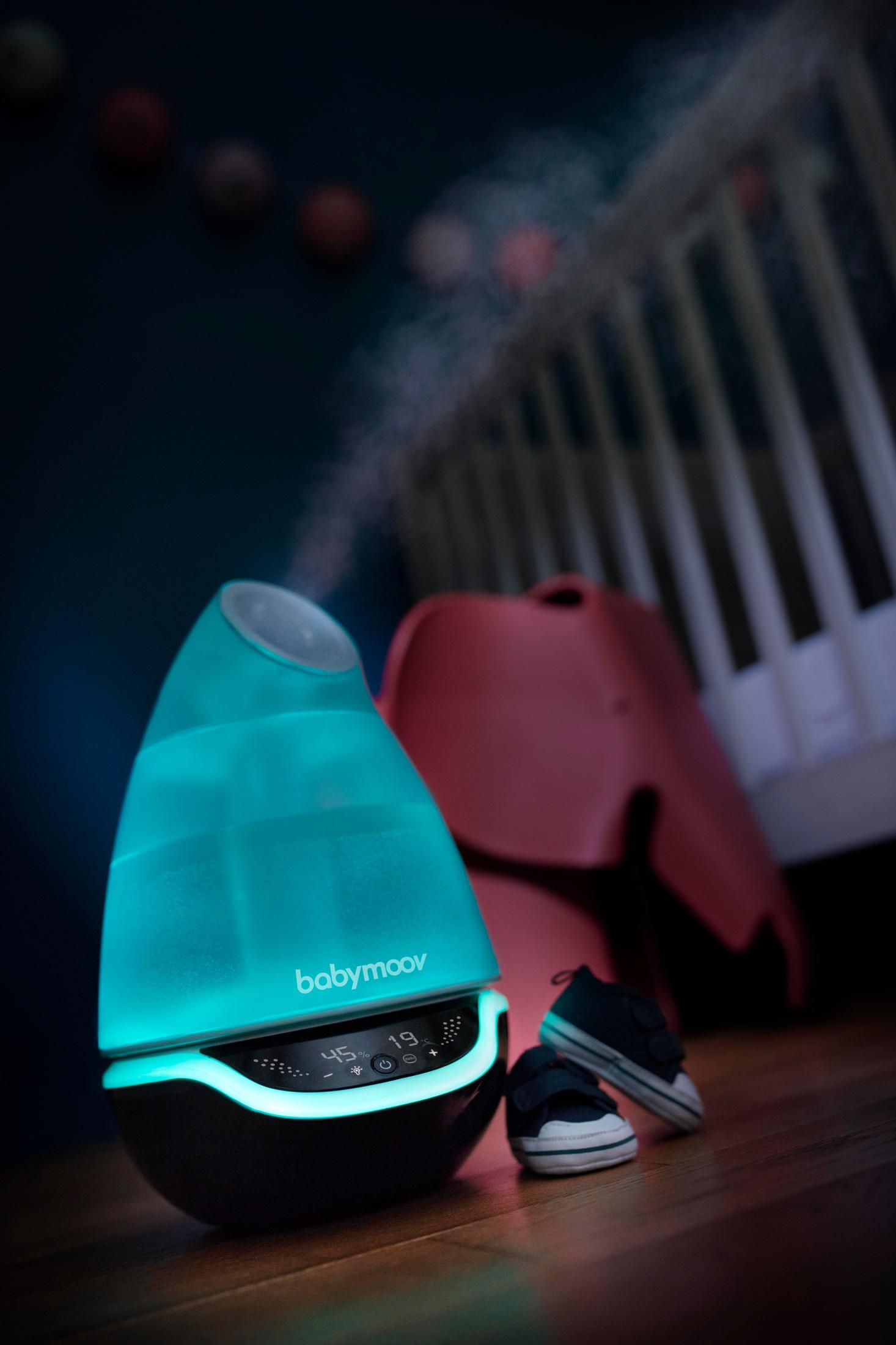 Ein blauer Luftbefeuchter mit einem digitalen Display und Nebel. Daneben ein Paar Babyschuhe.