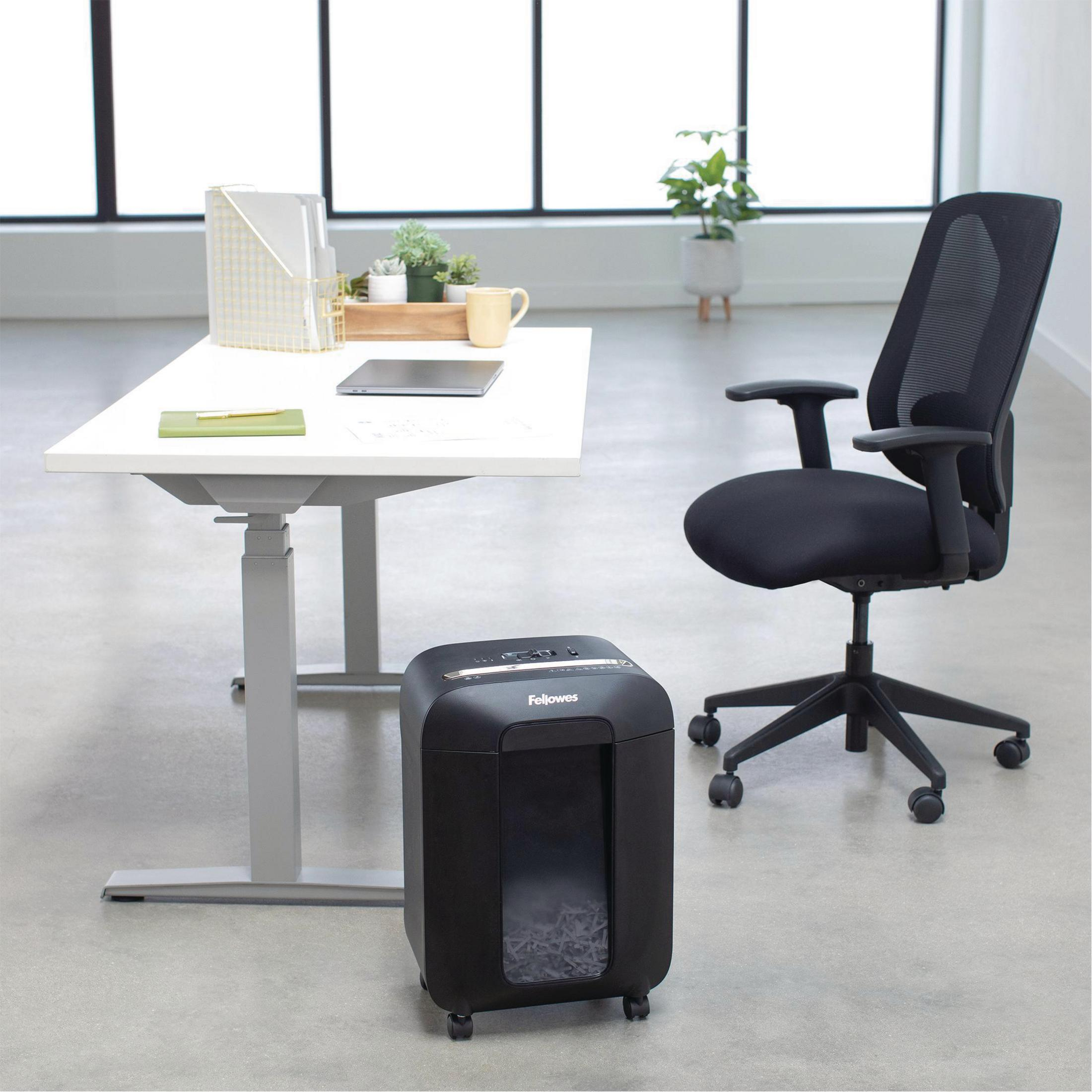 Scène de bureau avec bureau blanc, déchiqueteuse noire et chaise en maille noire. Plantes en pot visibles.