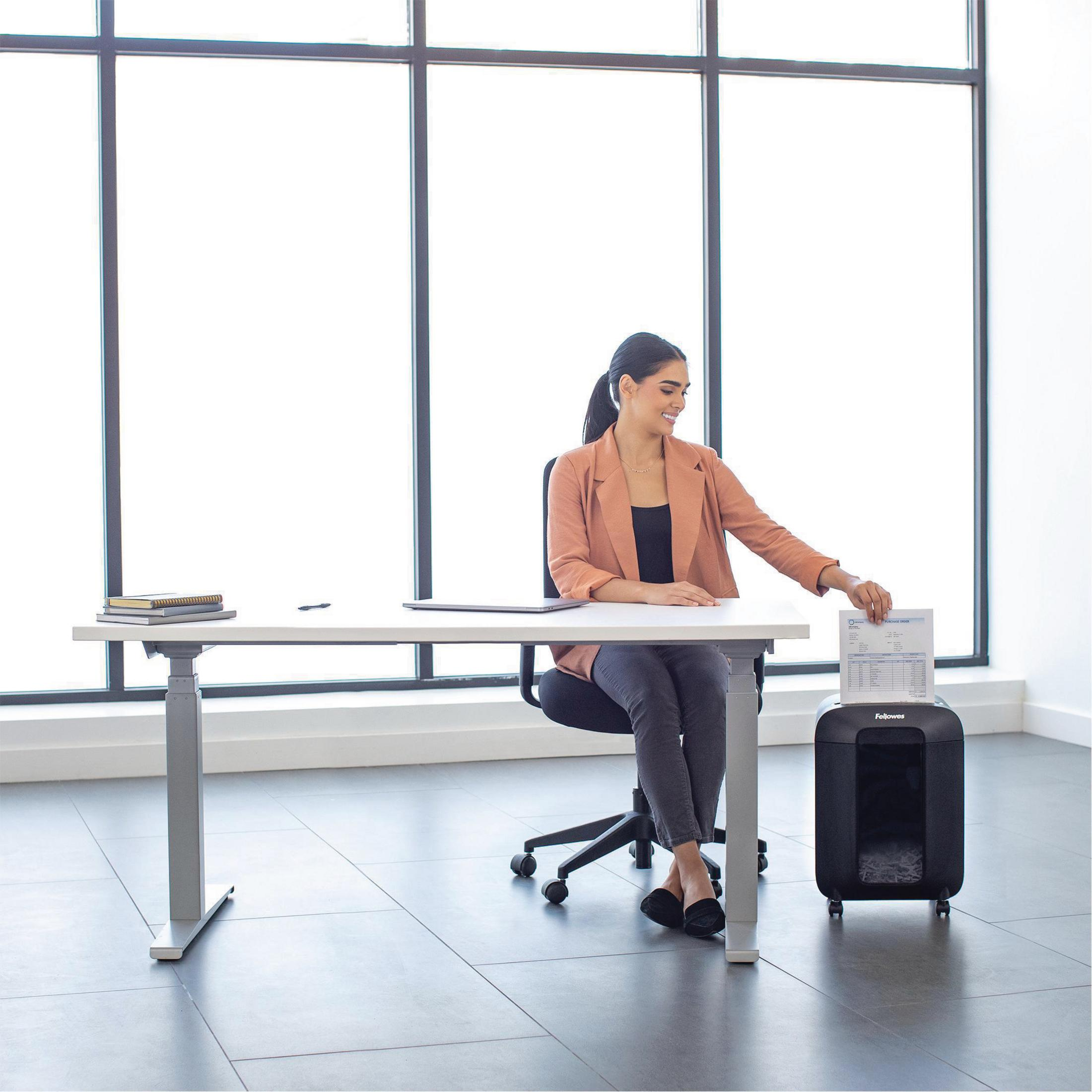Femme déchiquette des documents à un bureau devant une grande fenêtre.