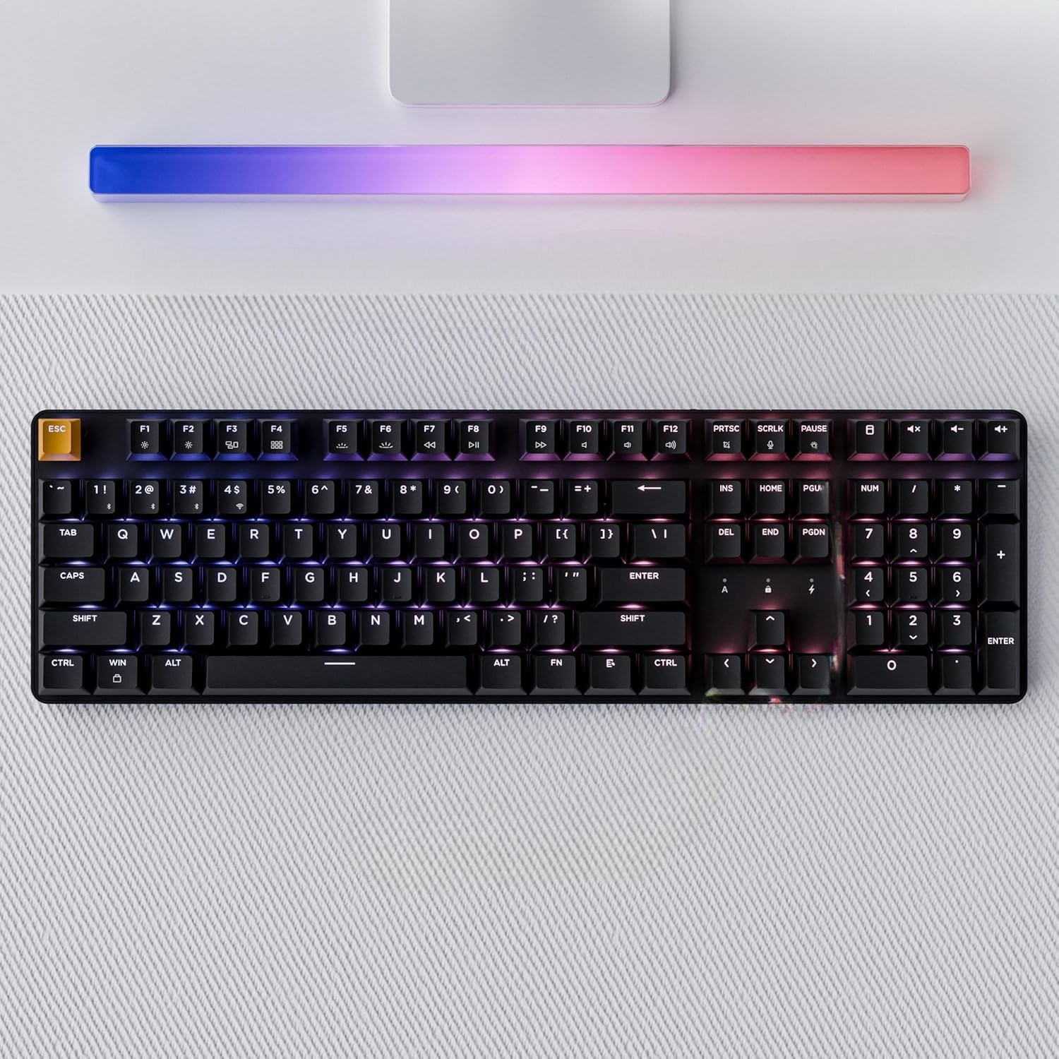 Czarna klawiatura mechaniczna z podświetleniem RGB, nad nią listwa świetlna w gradacji od niebieskiego do różowego.