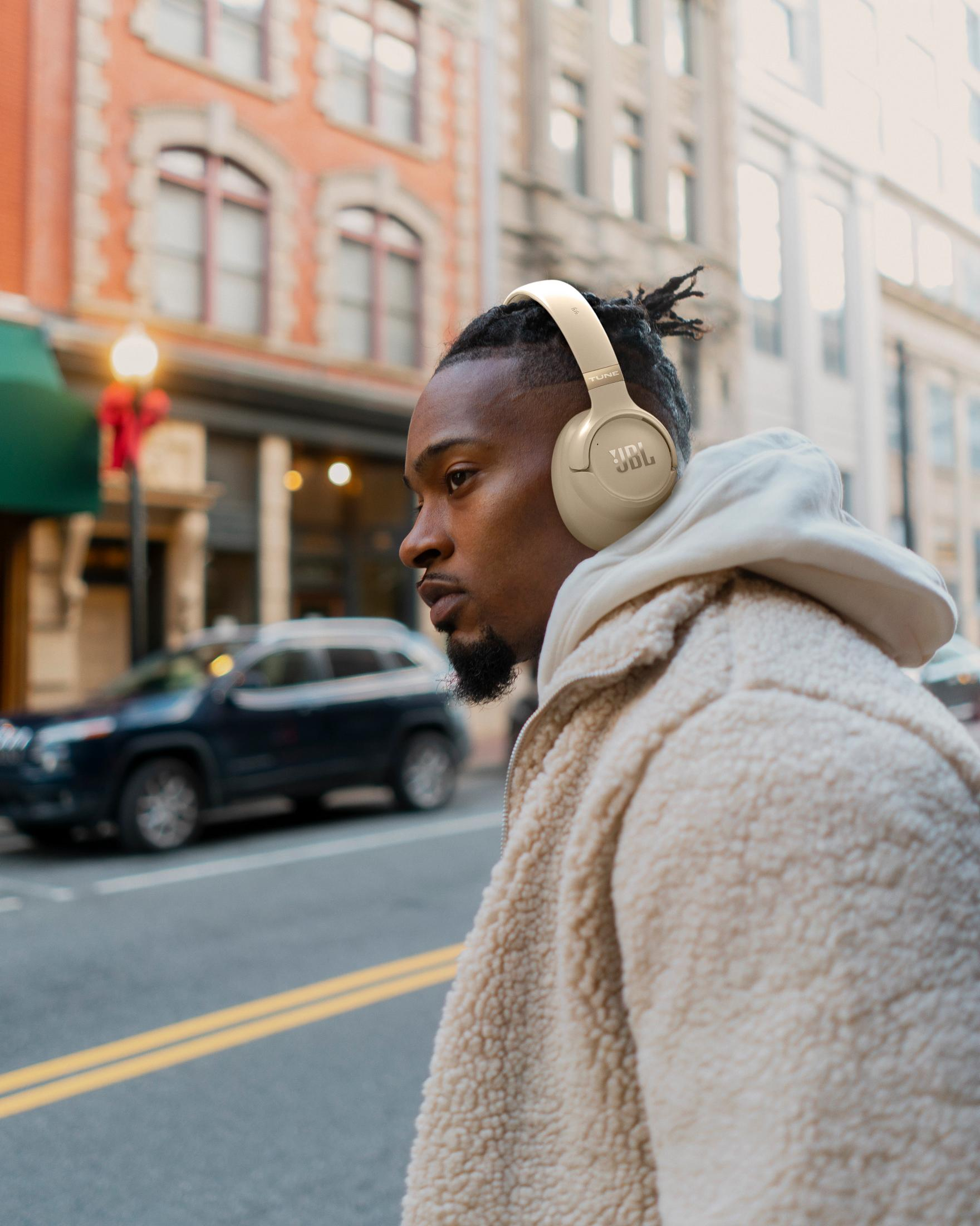 Uomo con cuffie cammina per strada. Indossa una giacca beige.