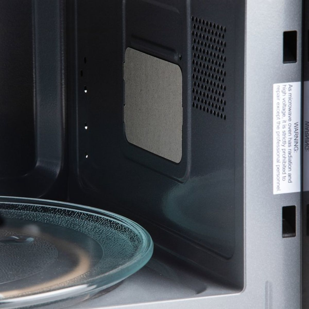 Intérieur d'un micro-ondes avec plateau en verre et étiquette d'avertissement.