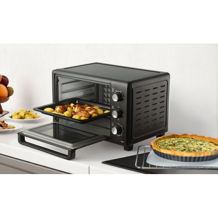 Ein schwarzer Tischbackofen mit gebratenem Hähnchen und Kartoffeln auf einem Blech und einer Quiche daneben.