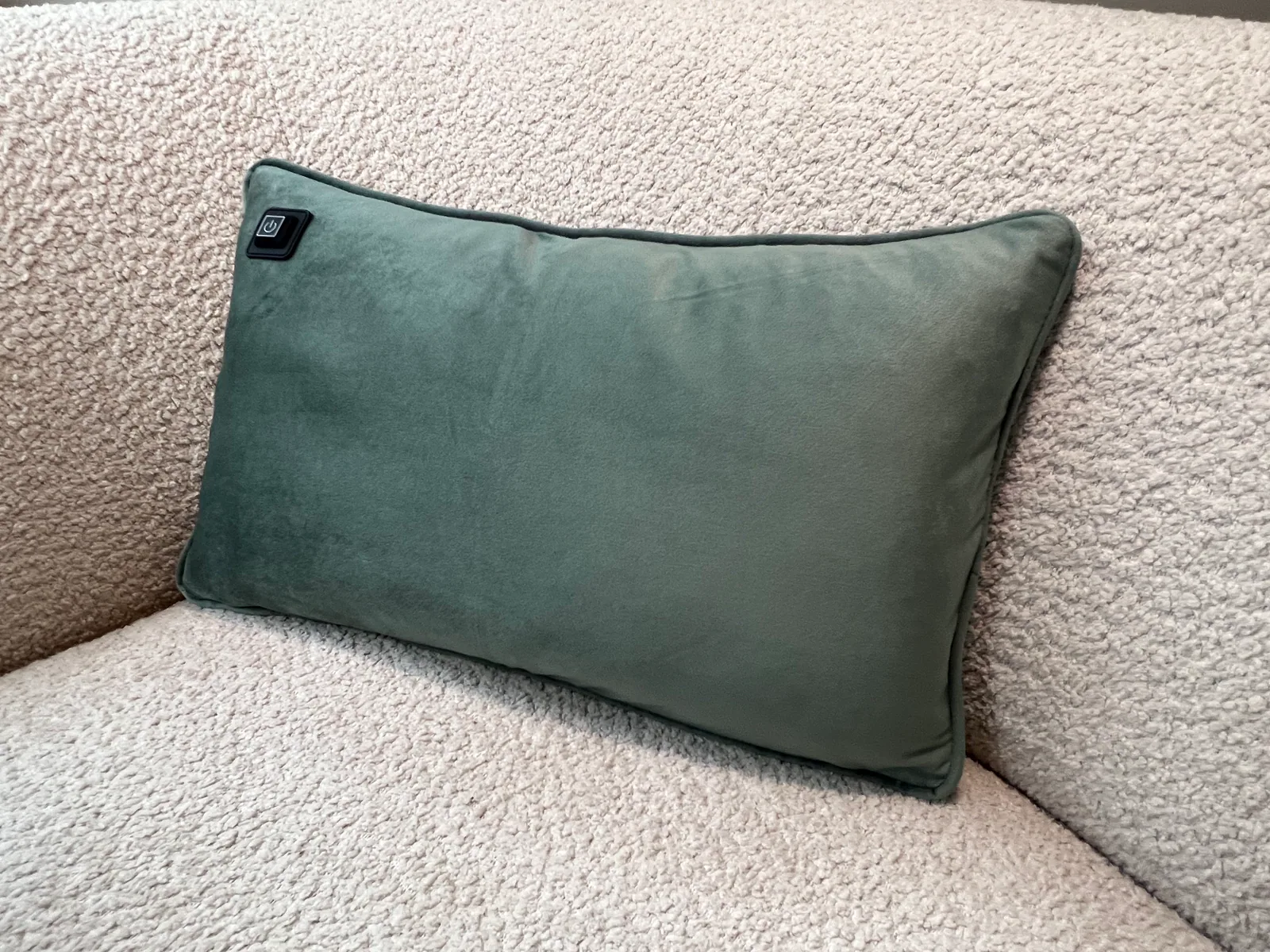 Ein grünes Kissen mit einem Power-Symbol-Knopf auf einem hellen Bouclé-Sofa.