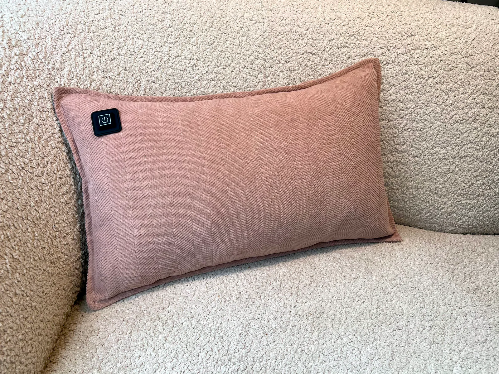 Ein rosafarbener Kissen mit einem Pfeilmuster und einem schwarzen Knopf, auf einem strukturierten Sofa.