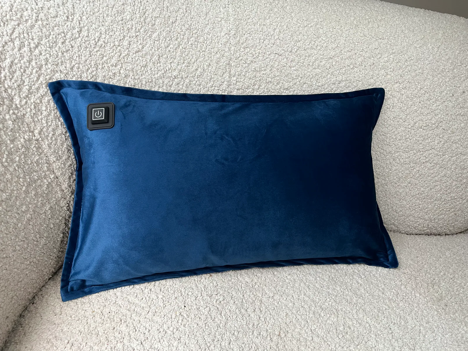 Ein dunkelblauer Kissen mit einem Ein-/Ausschaltknopf liegt auf einem cremefarbenen, strukturierten Sofa.