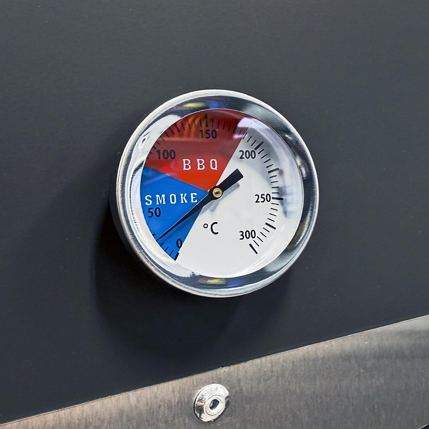 Ein Thermometer mit Skalen für Rauch und BBQ auf einem dunklen Grill.