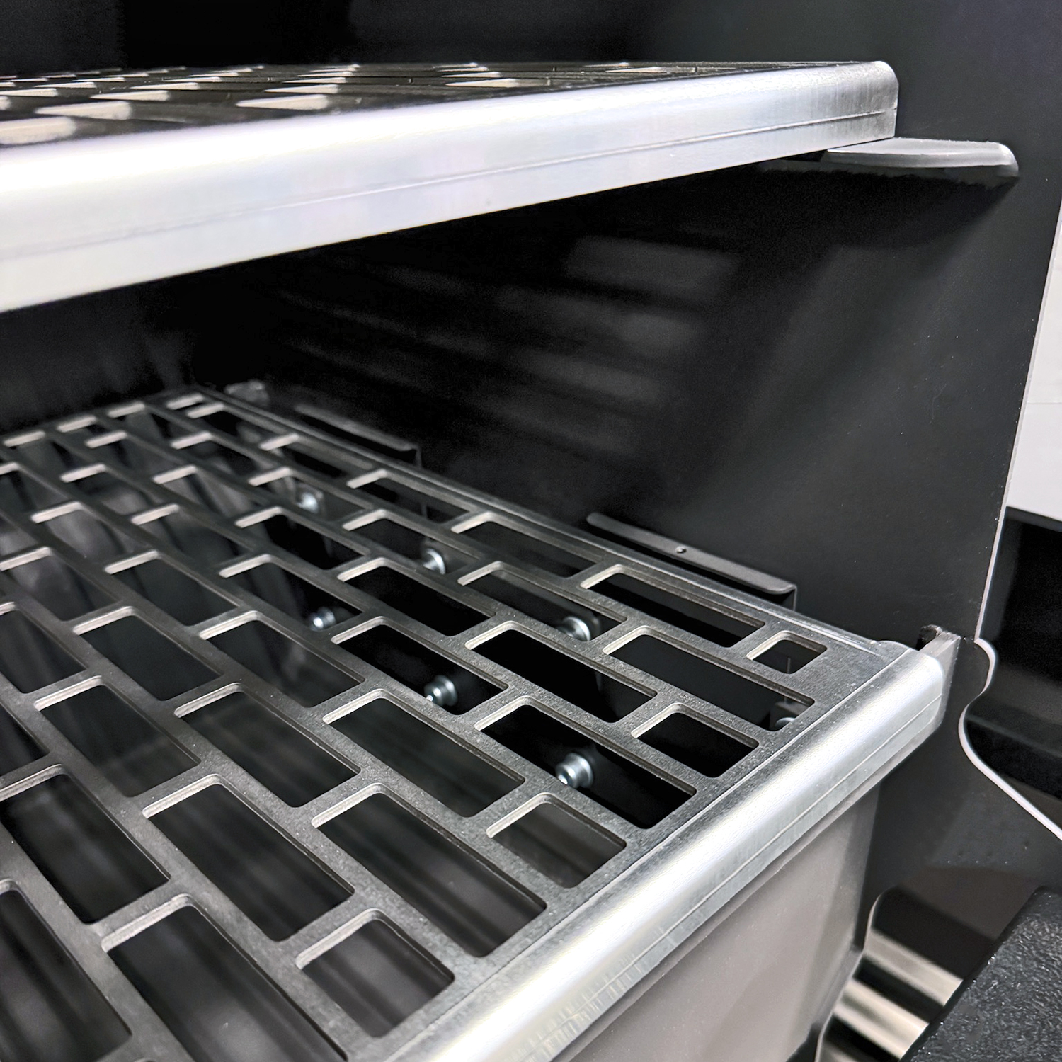 Ein Metallrost mit rechteckigen Öffnungen in einem schwarzen Gehäuse.