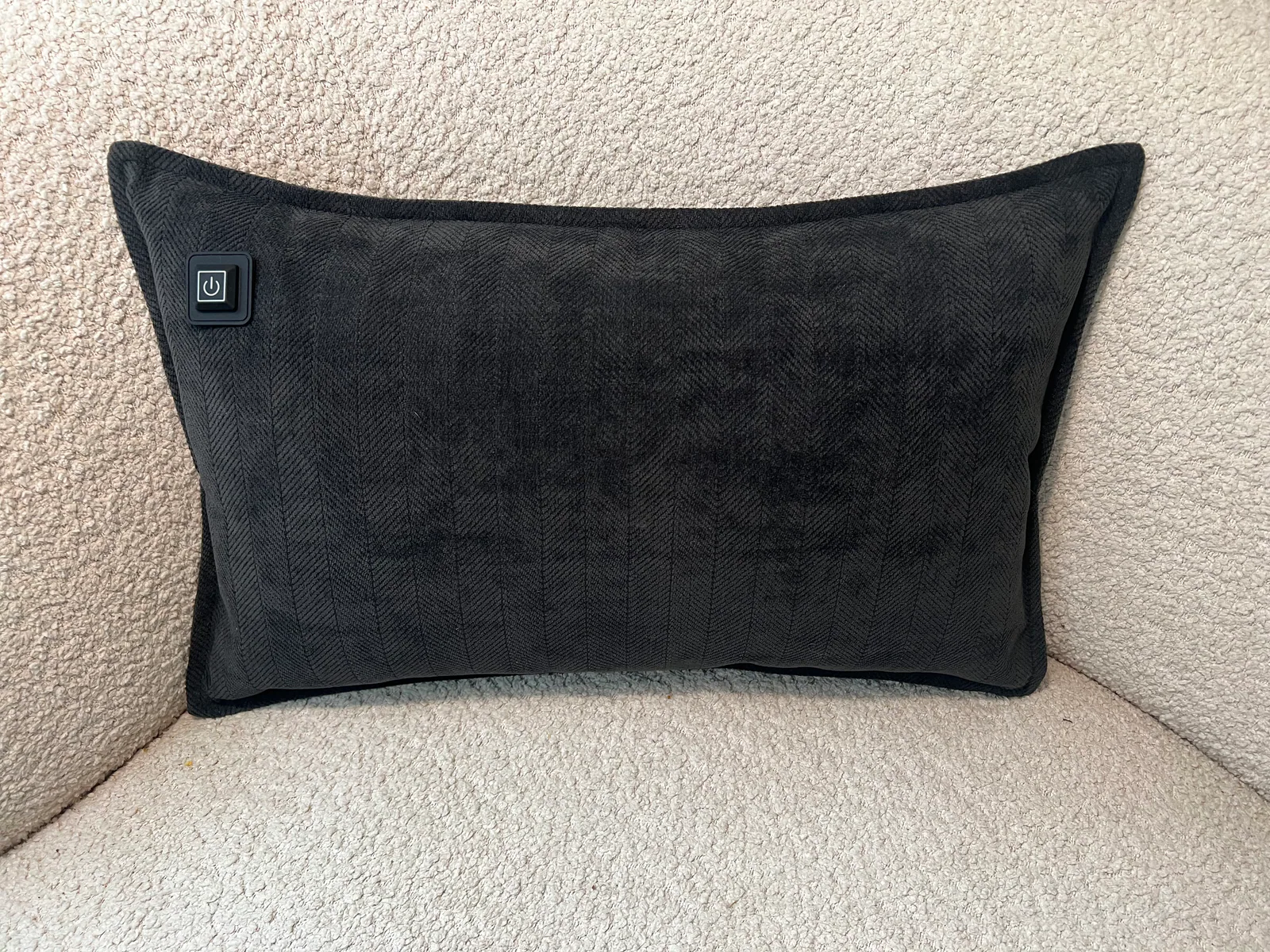 Schwarzes Kissen mit Fischgrätmuster und Power-Button auf einem cremefarbenen Stuhl.