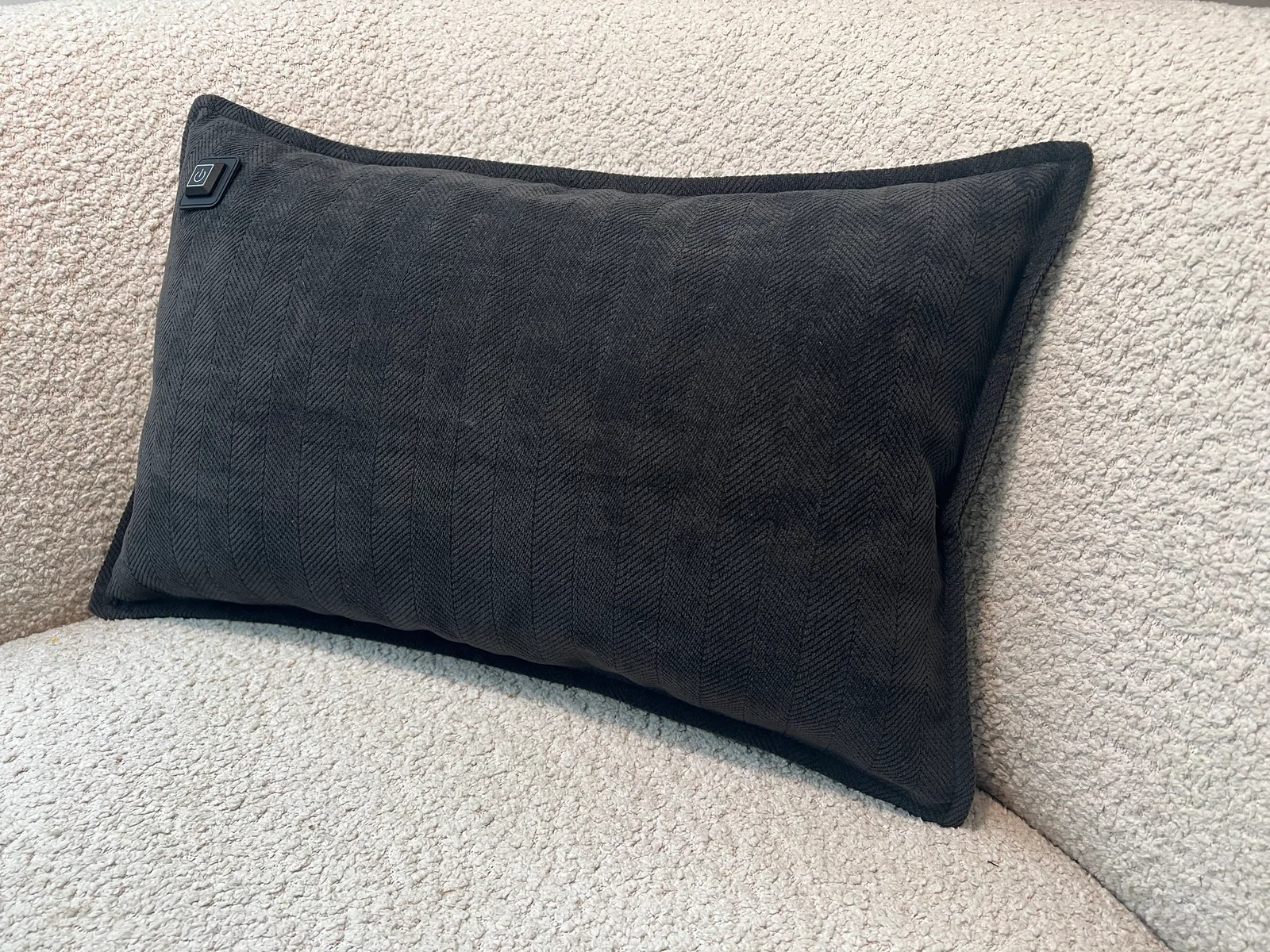 Dunkelgraues Kissen mit Fischgrätmuster auf einem cremefarbenen, flauschigen Sofa.