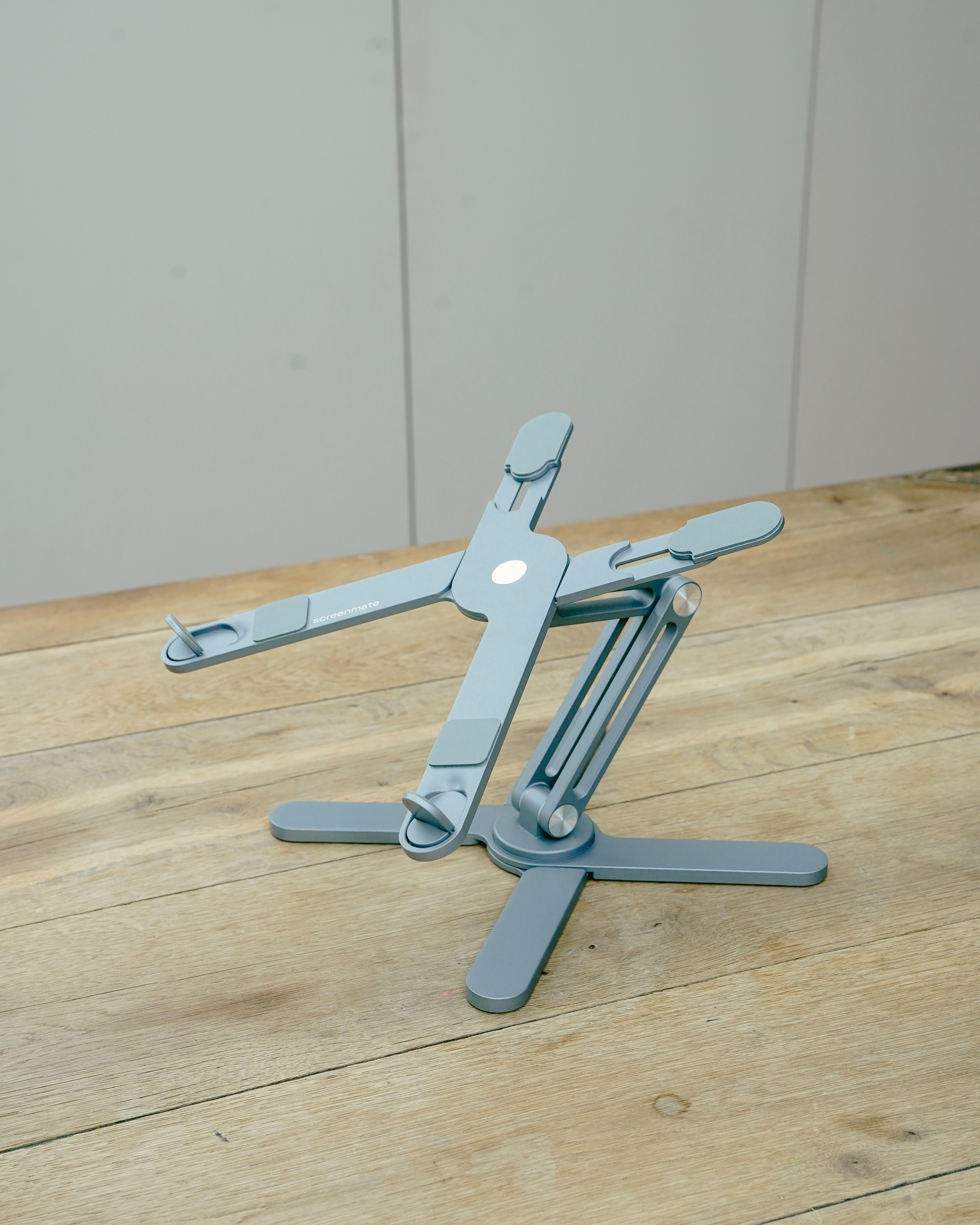Un support gris réglable pour ordinateur portable est sur une table en bois. Le support a un logo.