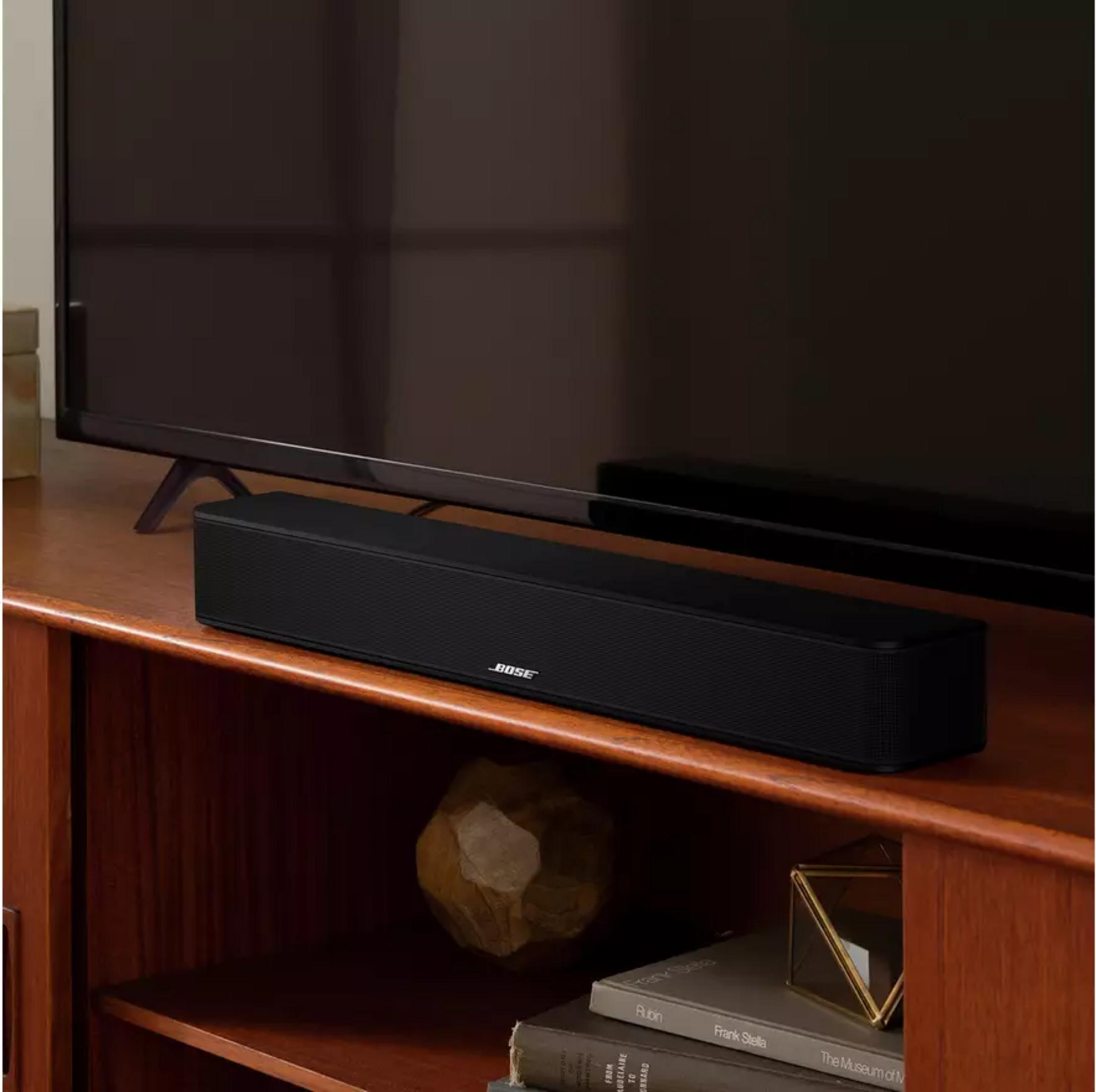 Barra de sonido Bose negra frente a un televisor en un mueble de madera.