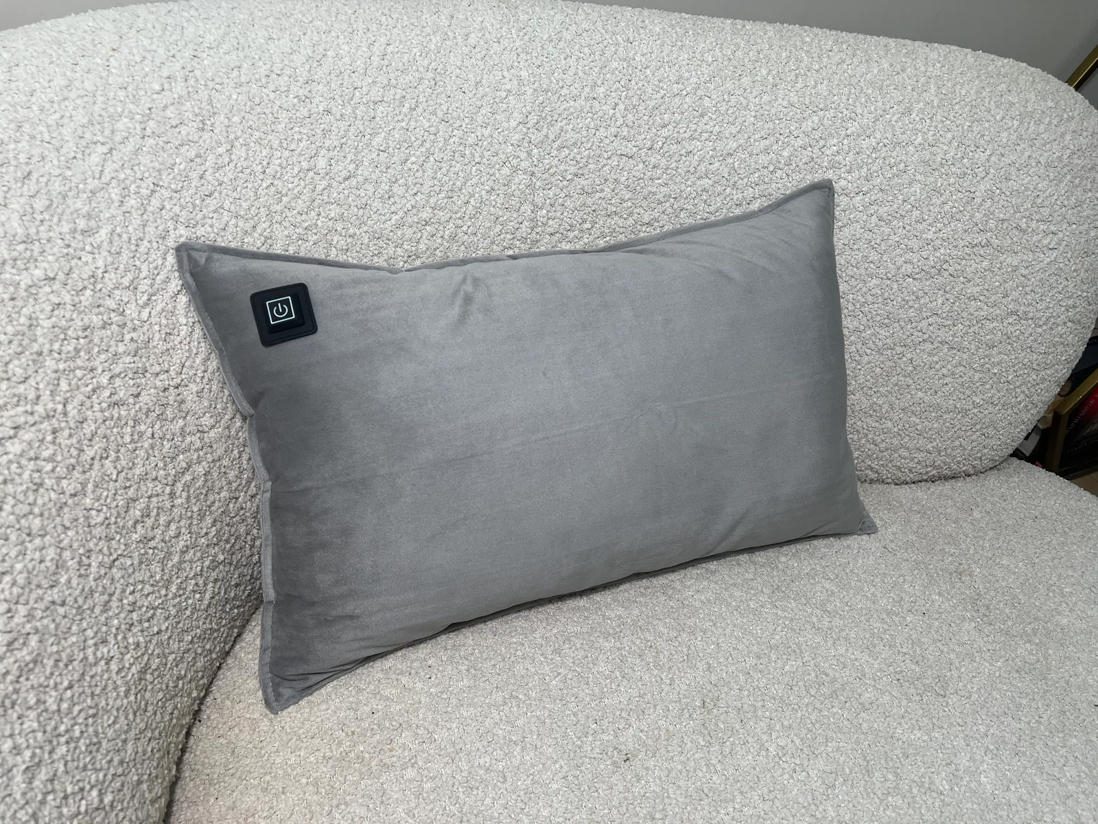 Ein graues Samtkissen mit Power-Knopf sitzt auf einer cremefarbenen Couch.