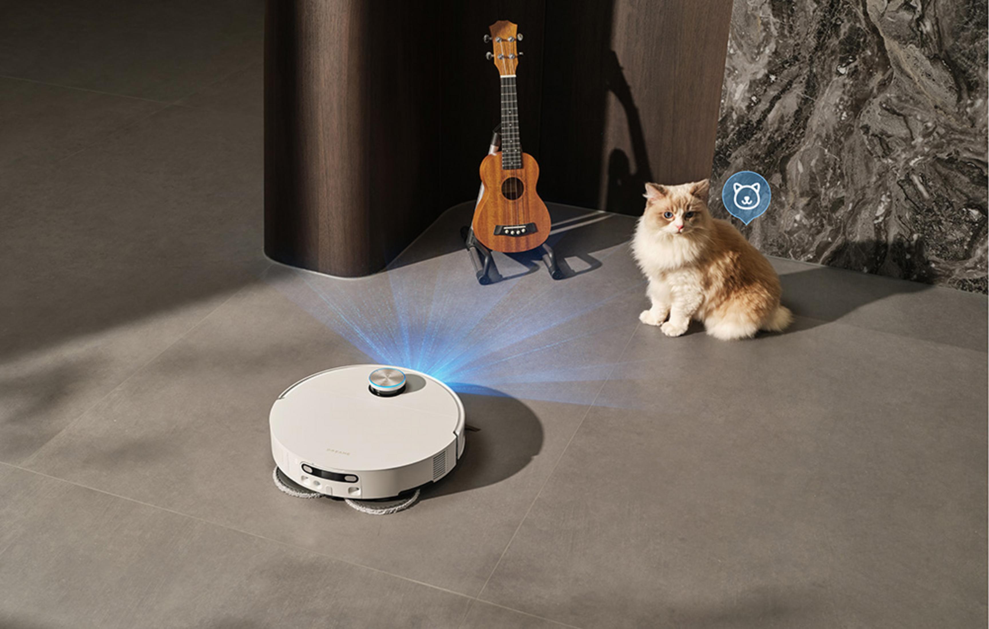 Un robot aspirapolvere bianco pulisce il pavimento accanto a un gatto e un'ukulele.