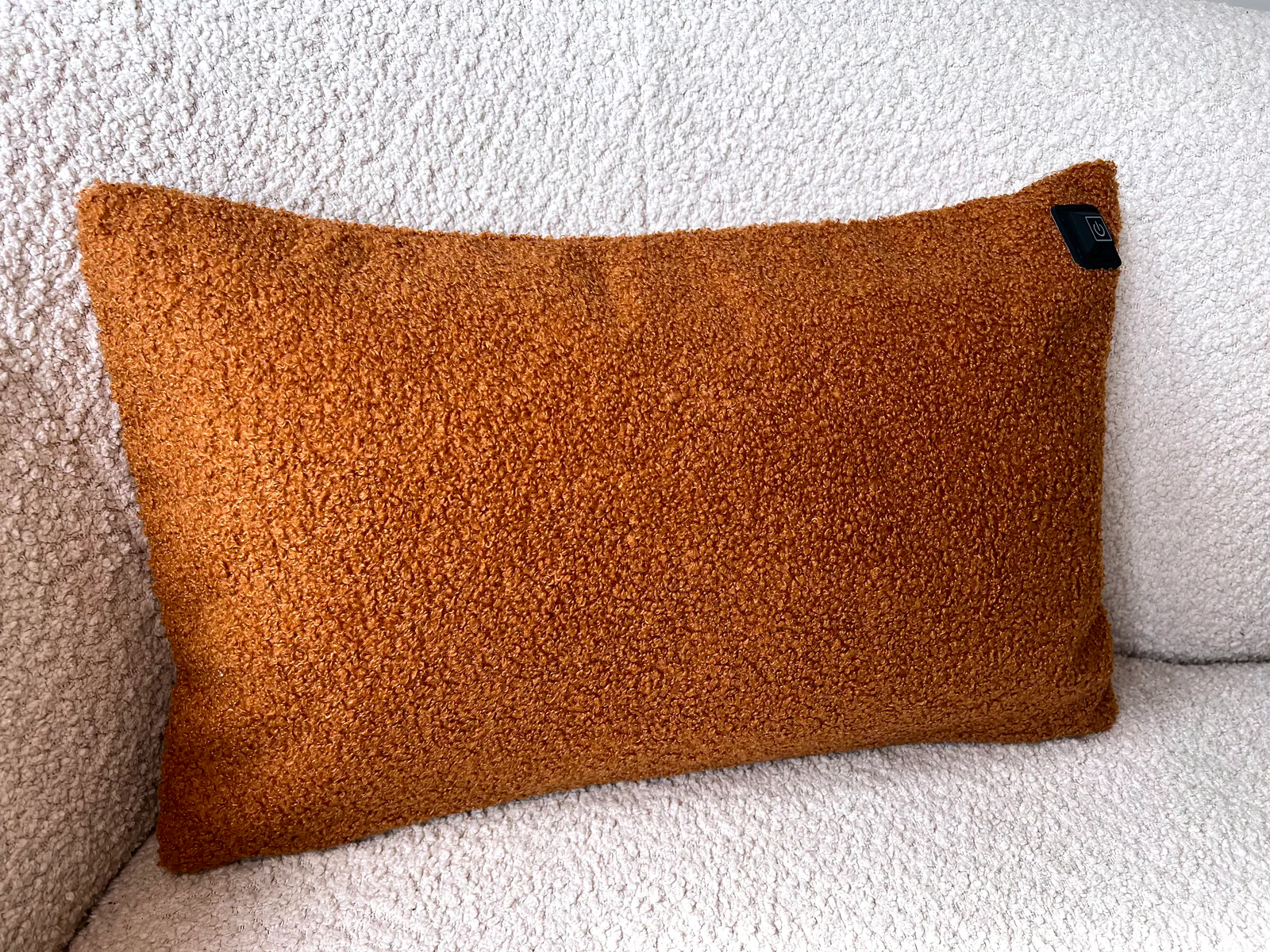 Ein orangefarbenes Teddy-Kissen liegt auf einem weißen Bouclé-Sofa.