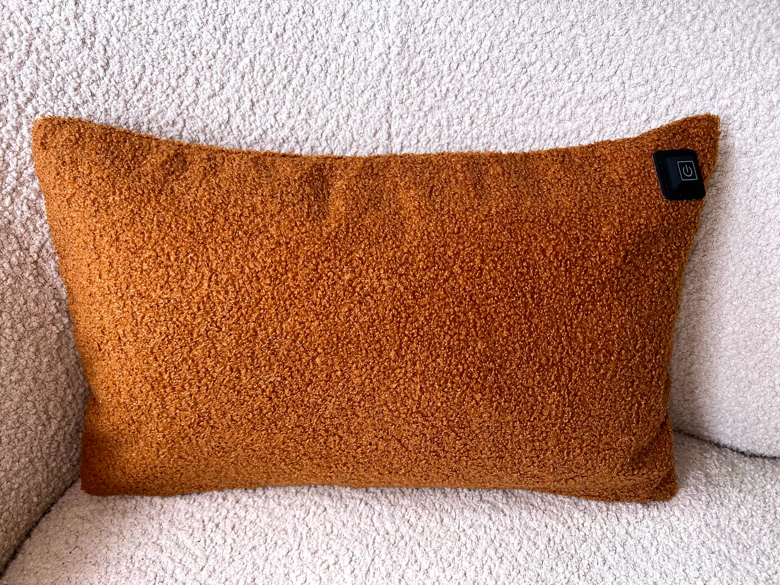 Ein orangefarbenes Kissen mit Teddyfell-Textur und einem schwarzen Ein-/Ausschaltknopf.