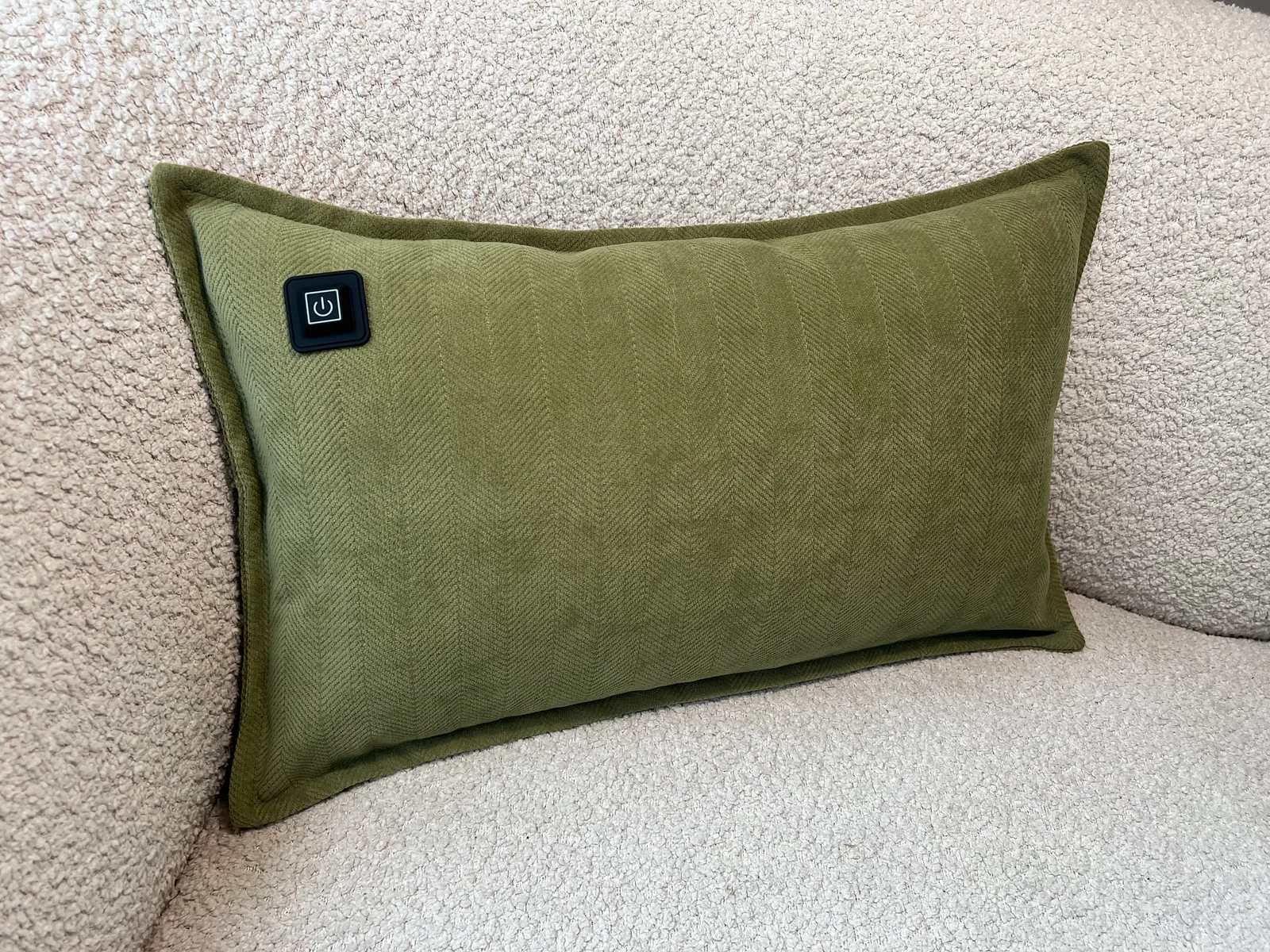Ein grünes Kissen mit Fischgrätmuster und einem schwarzen Power-Symbol liegt auf einem hellen Sofa.