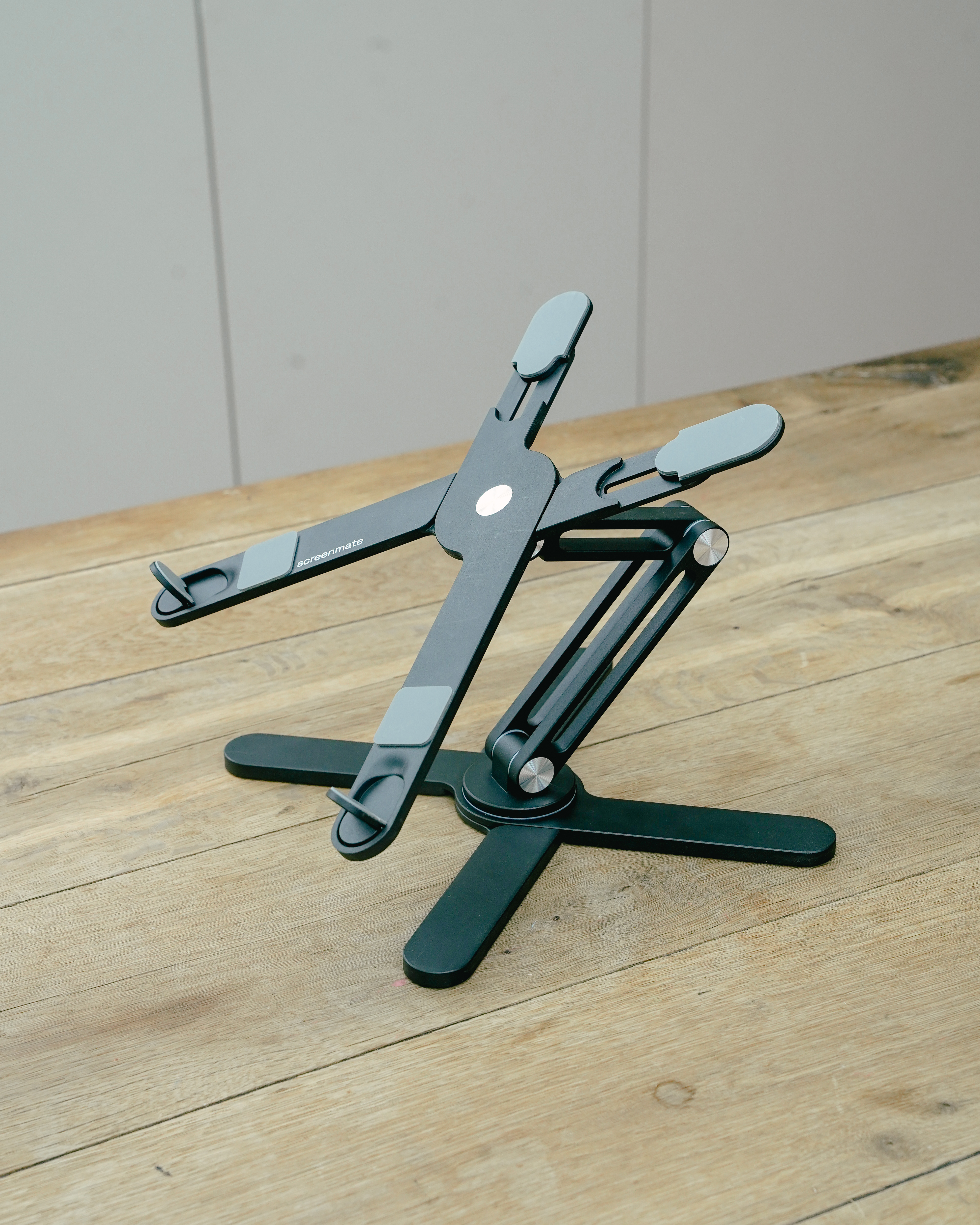 Un support d'ordinateur portable réglable gris foncé à base large est sur bois.