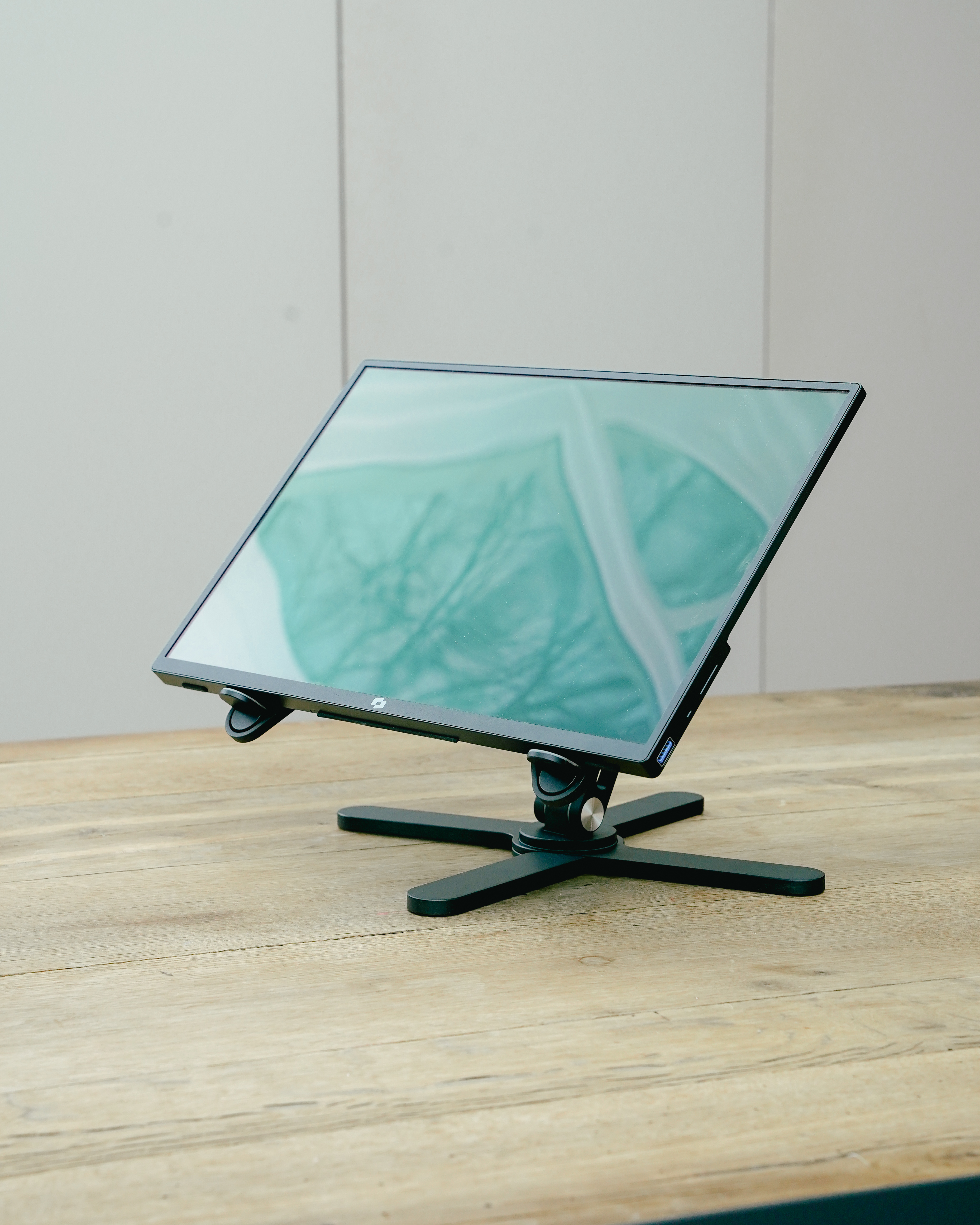 Un moniteur noir sur un support noir, posé sur une table en bois.