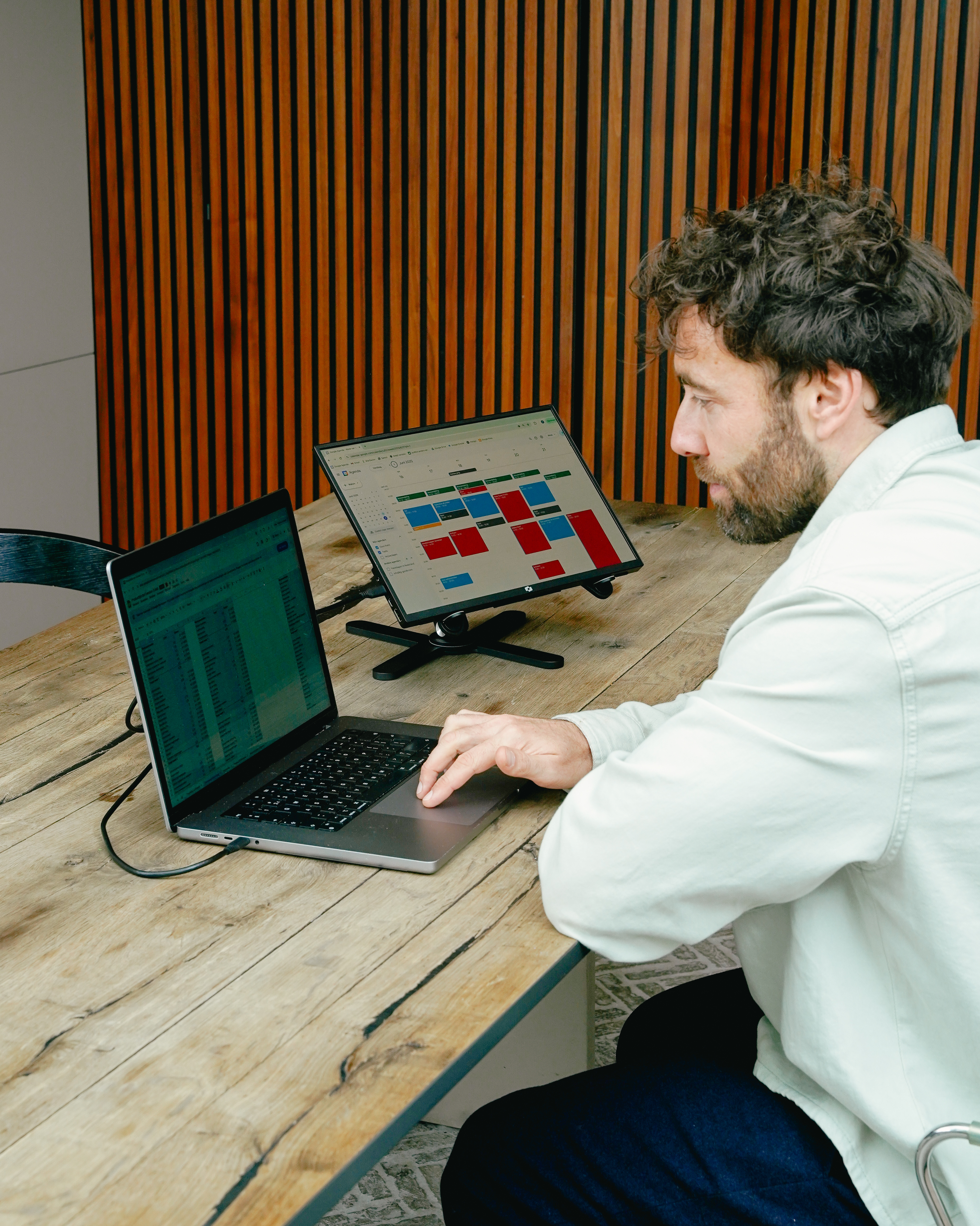 Homme travaillant sur un ordinateur portable et un moniteur affichant un calendrier.